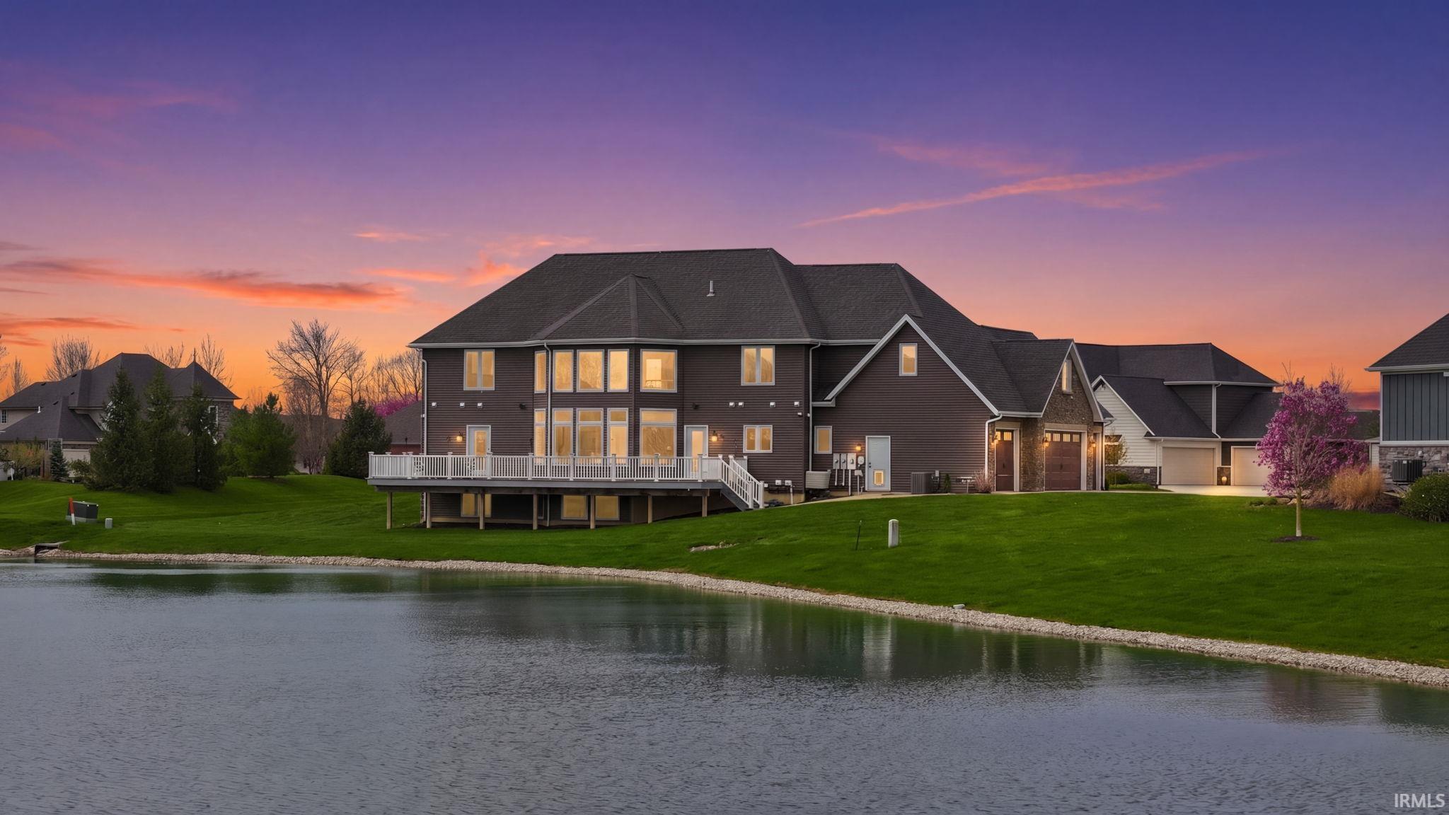 Rear view of house featuring a deck with water view, a yard, and driveway