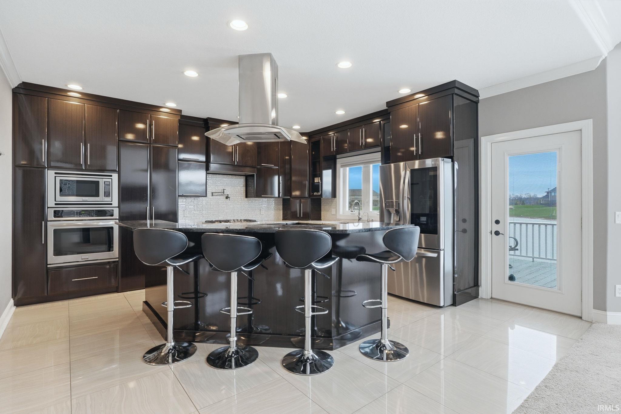 Kitchen featuring light tile patterned floors, island range hood, stainless steel appliances, crown molding, and backsplash