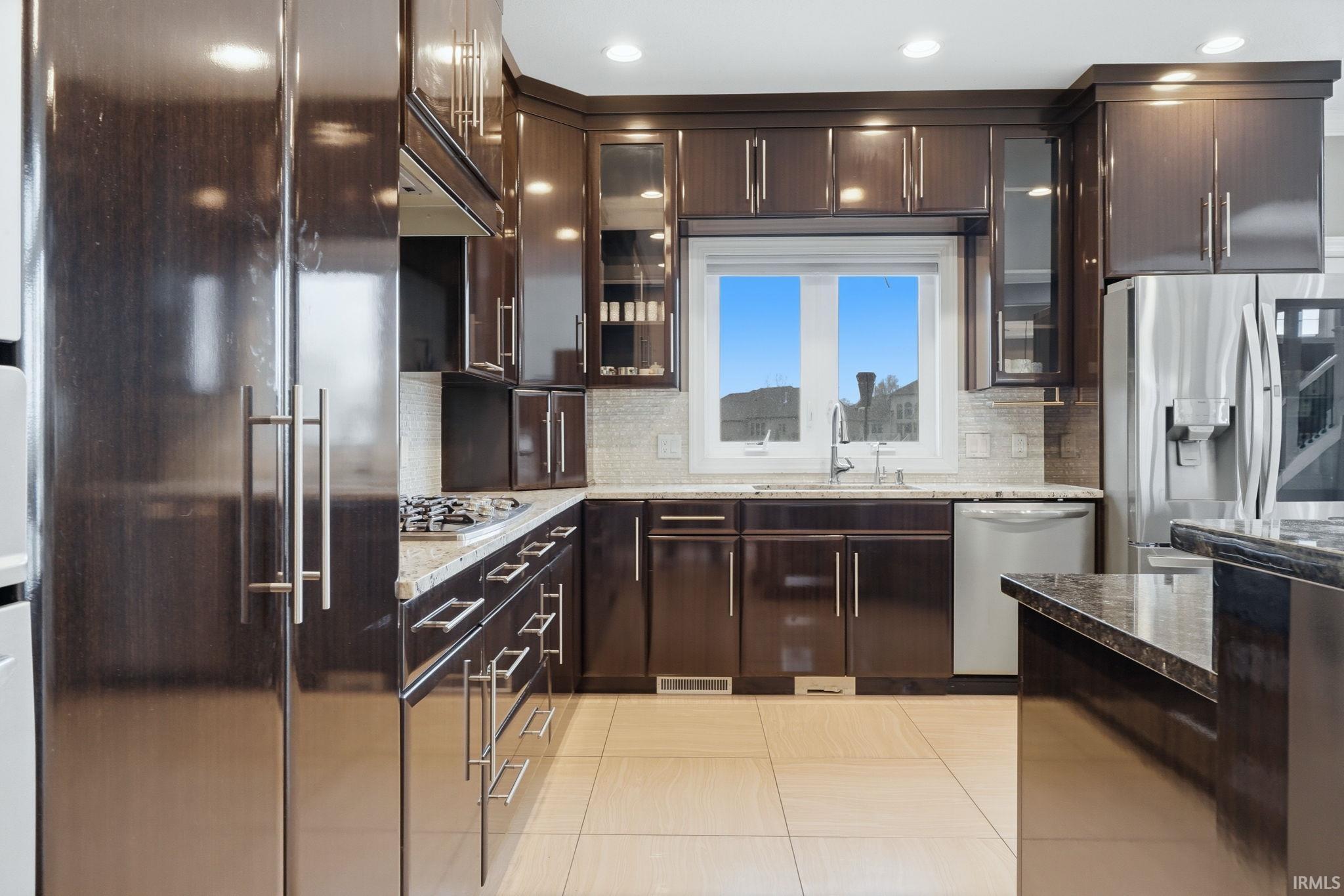 Kitchen featuring dark wood finish cabinetry, stainless steel appliances, dark stone countertops, and glass insert cabinets