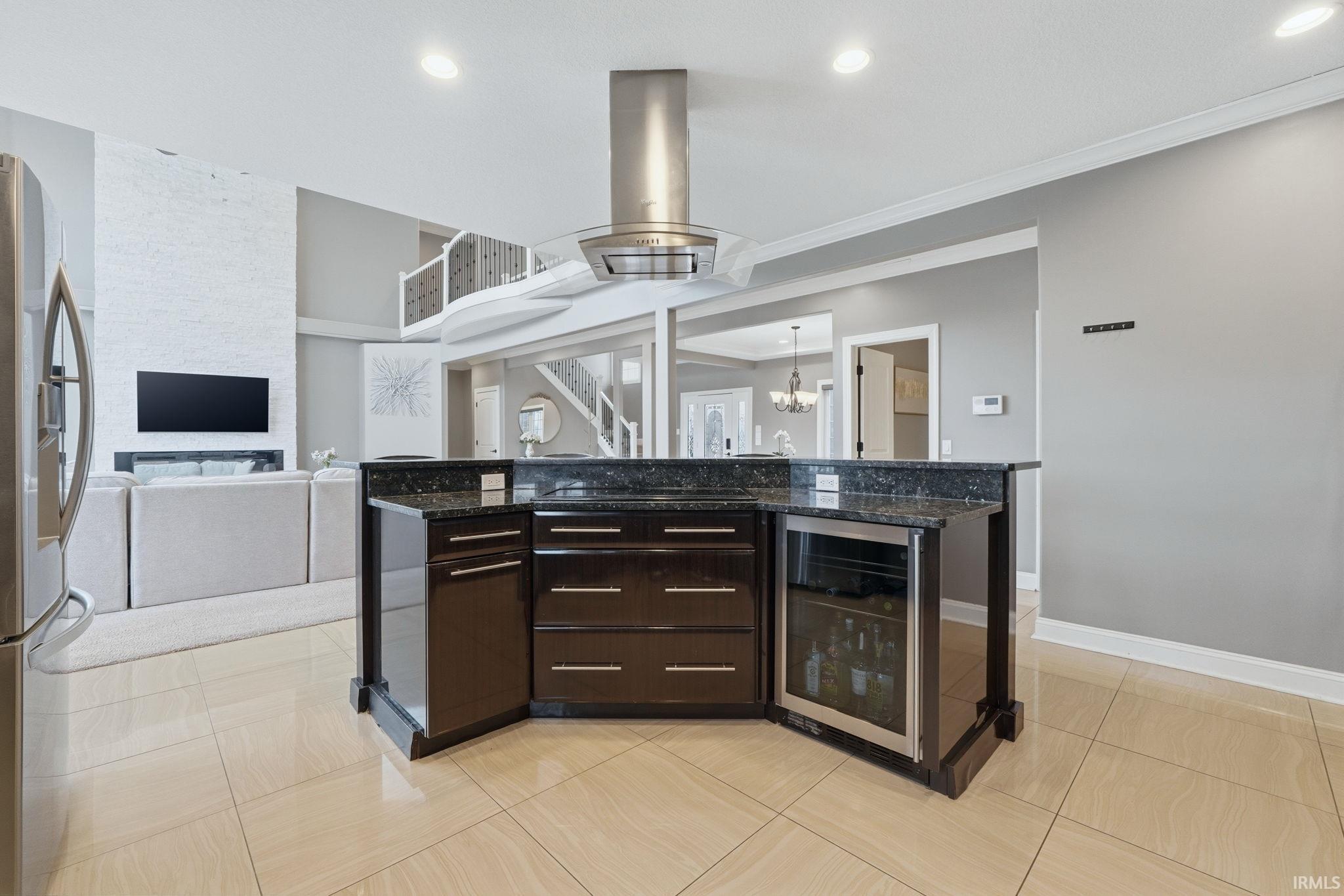 Kitchen featuring dark wood finish cabinetry, a kitchen island, wine cooler, stainless steel refrigerator with ice dispenser, and open floor plan