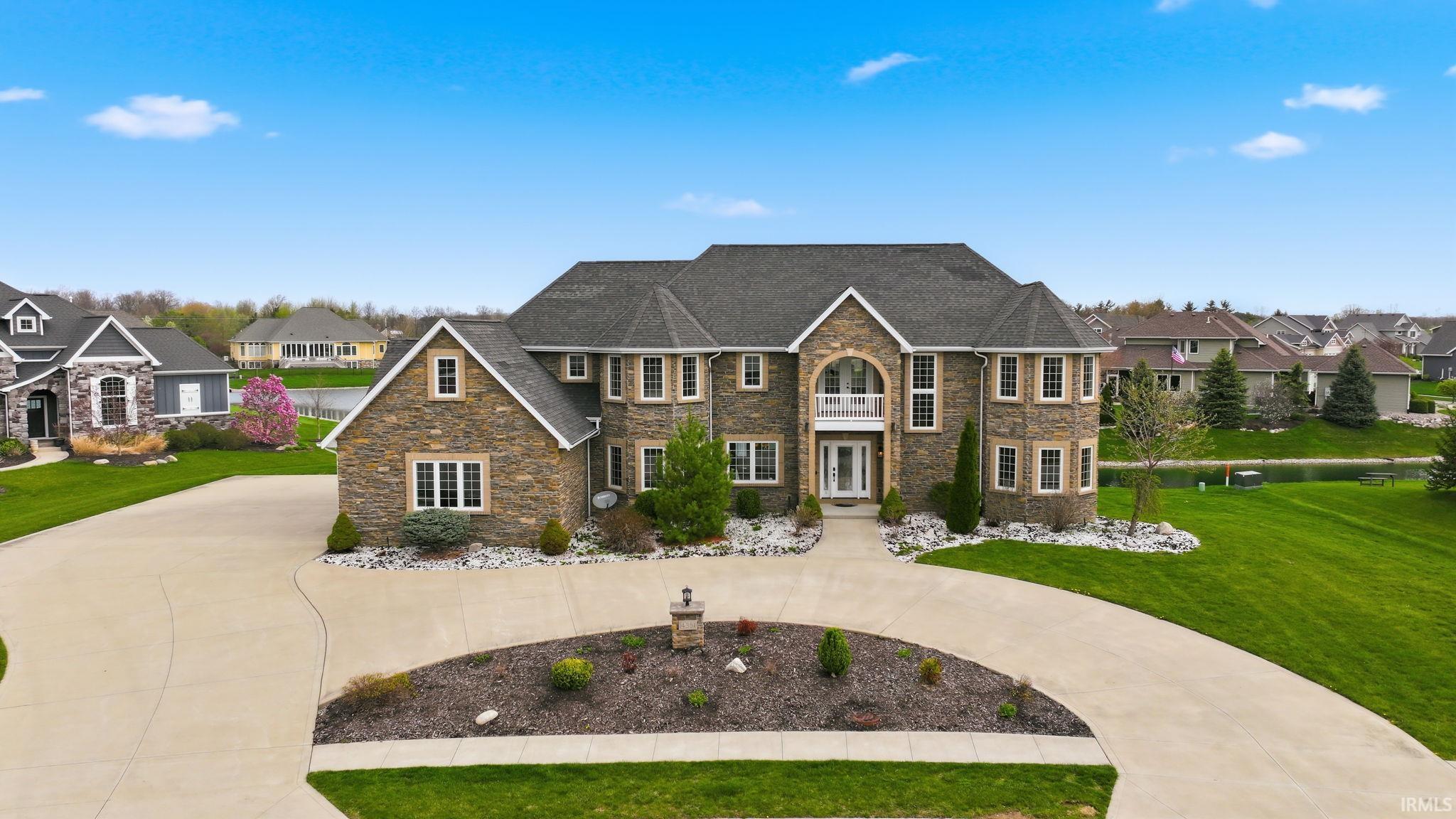 View of front of home with stone siding, a front yard, a residential view, french doors, and curved driveway