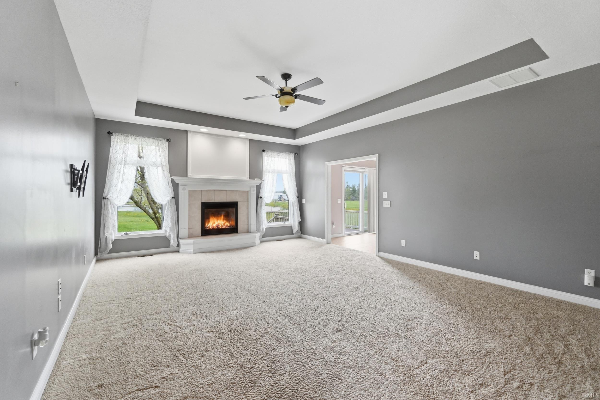 Unfurnished living room with a tray ceiling, ceiling fan, a tiled fireplace, and light colored carpet