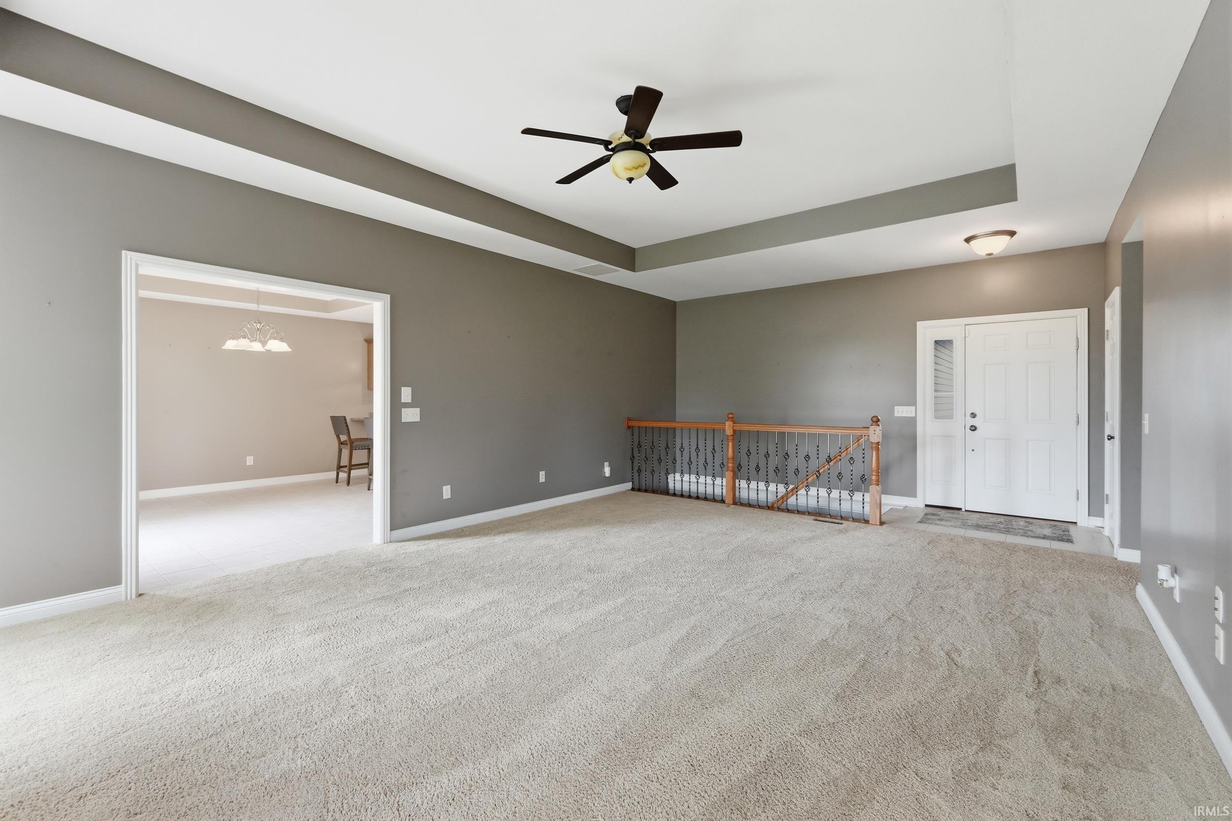 Spare room featuring a ceiling fan, light carpet, a chandelier, and a tray ceiling