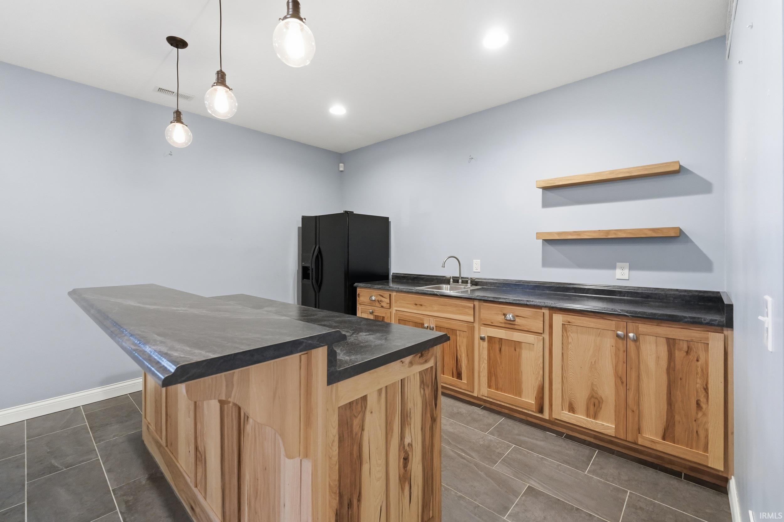 Kitchen featuring dark countertops, black refrigerator with ice dispenser, open shelves, a center island, and hanging light fixtures