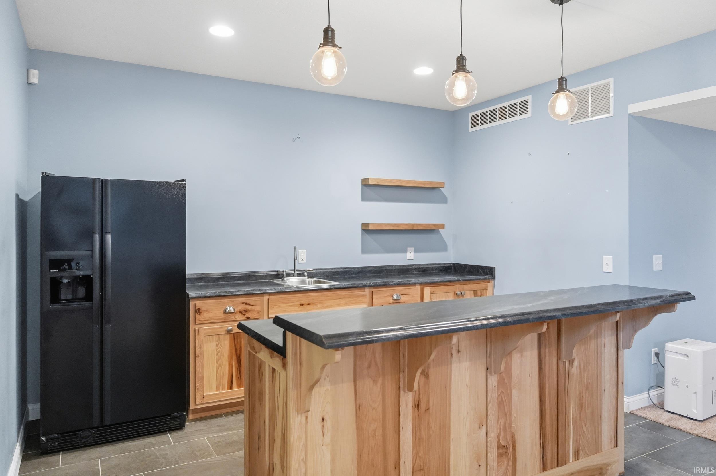 Kitchen featuring black fridge with ice dispenser, a breakfast bar area, decorative light fixtures, open shelves, and a peninsula