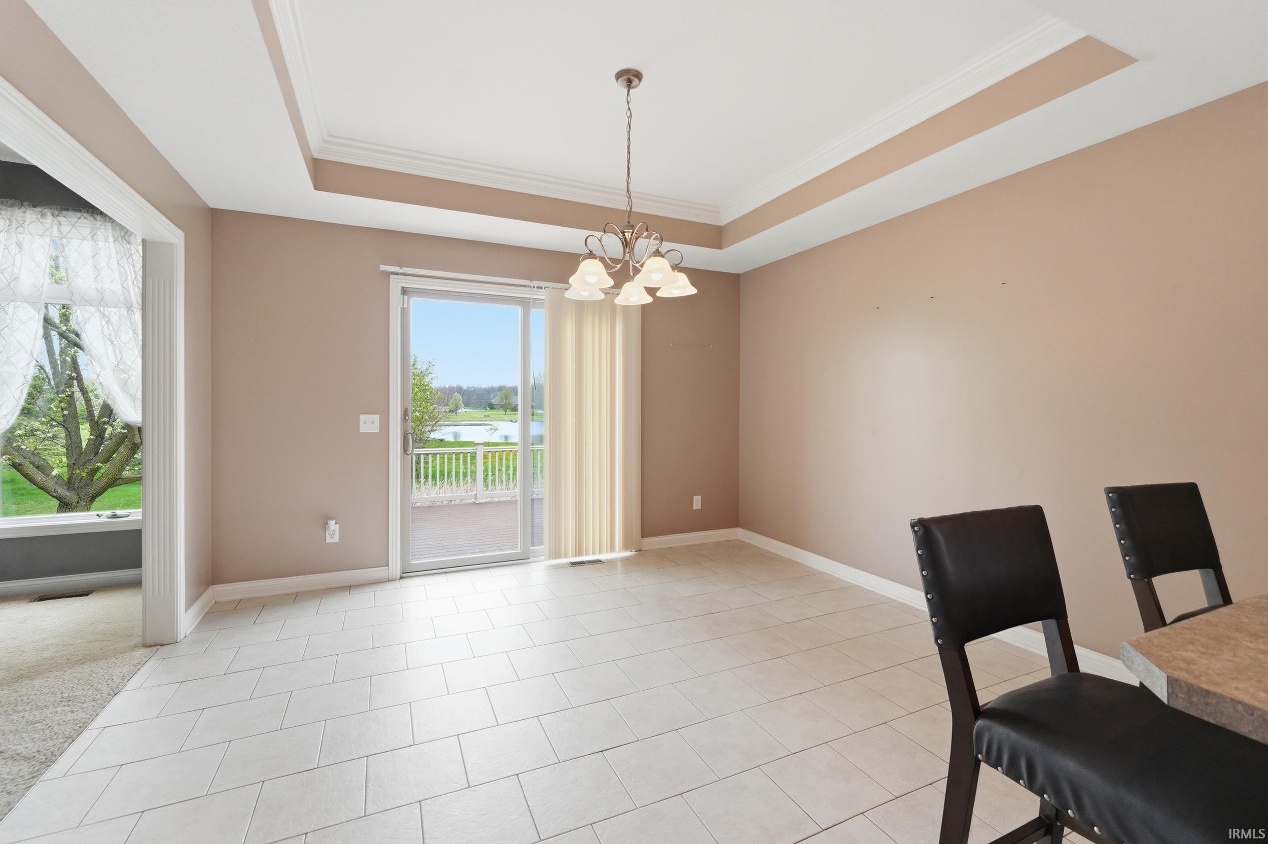 Unfurnished dining area featuring a chandelier, a tray ceiling, crown molding, and light tile patterned floors