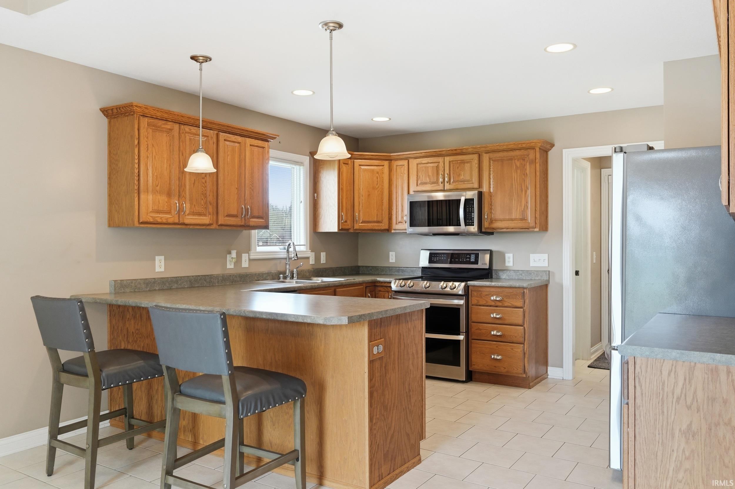 Kitchen with stainless steel appliances, a breakfast bar area, wood finish cabinetry, a peninsula, and pendant lighting