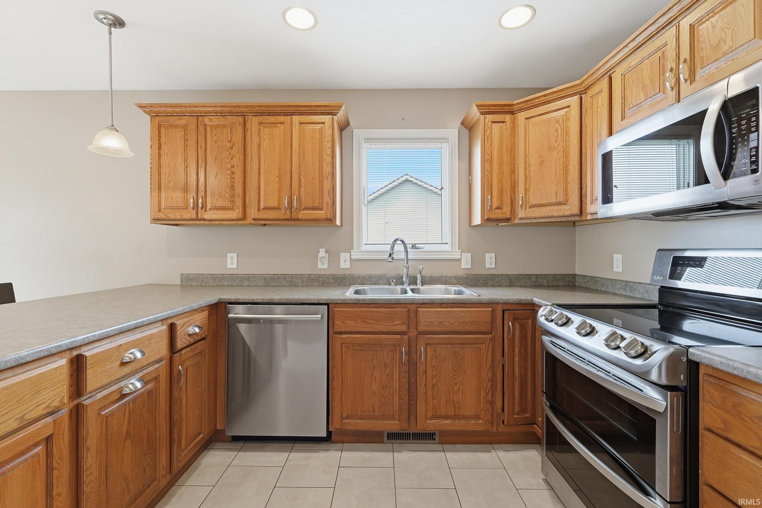 Kitchen featuring stainless steel appliances, pendant lighting, wood finish cabinetry, and light tile patterned floors