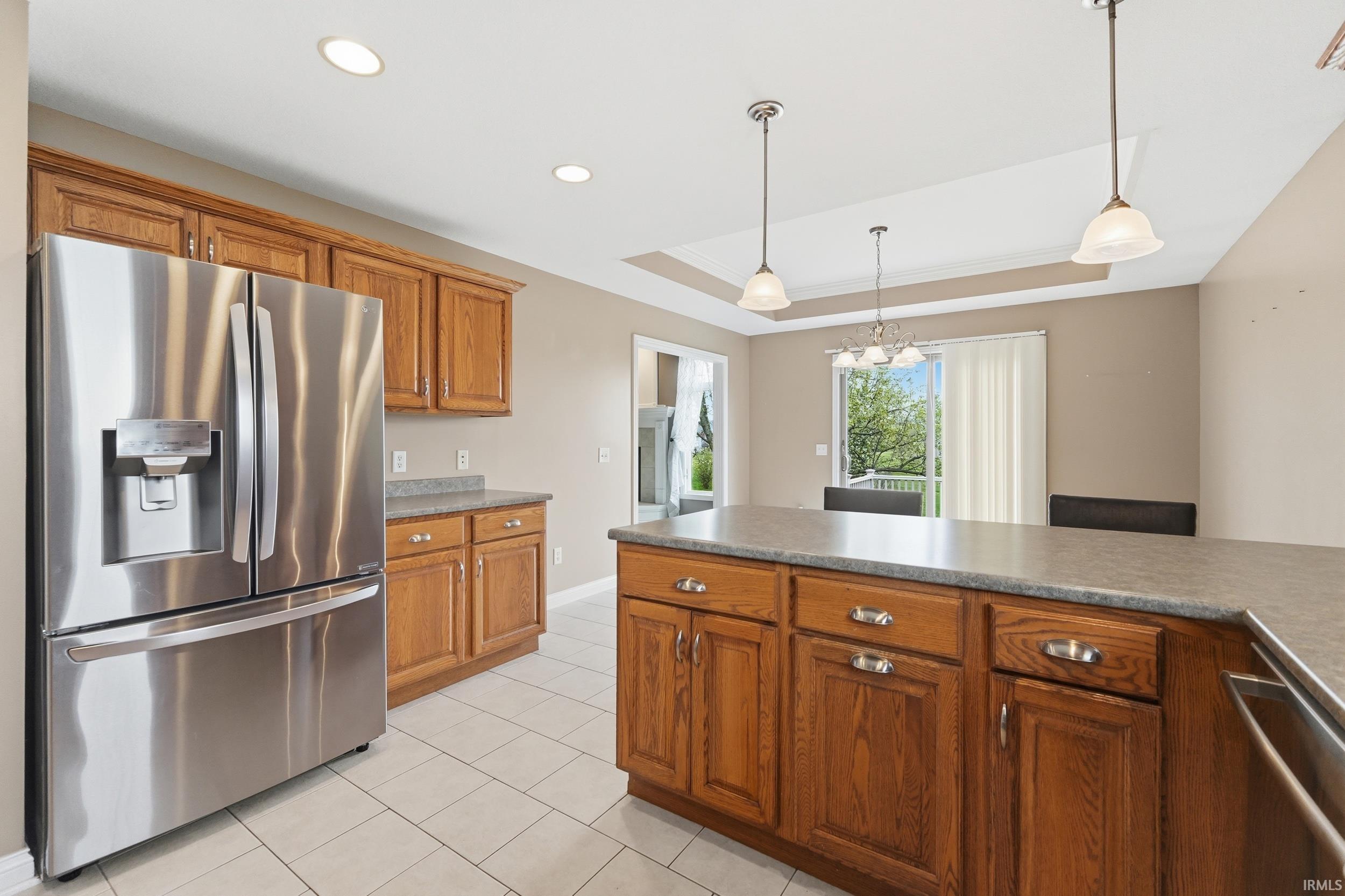 Kitchen with stainless steel appliances, a raised ceiling, wood finish cabinetry, hanging light fixtures, and light tile patterned flooring