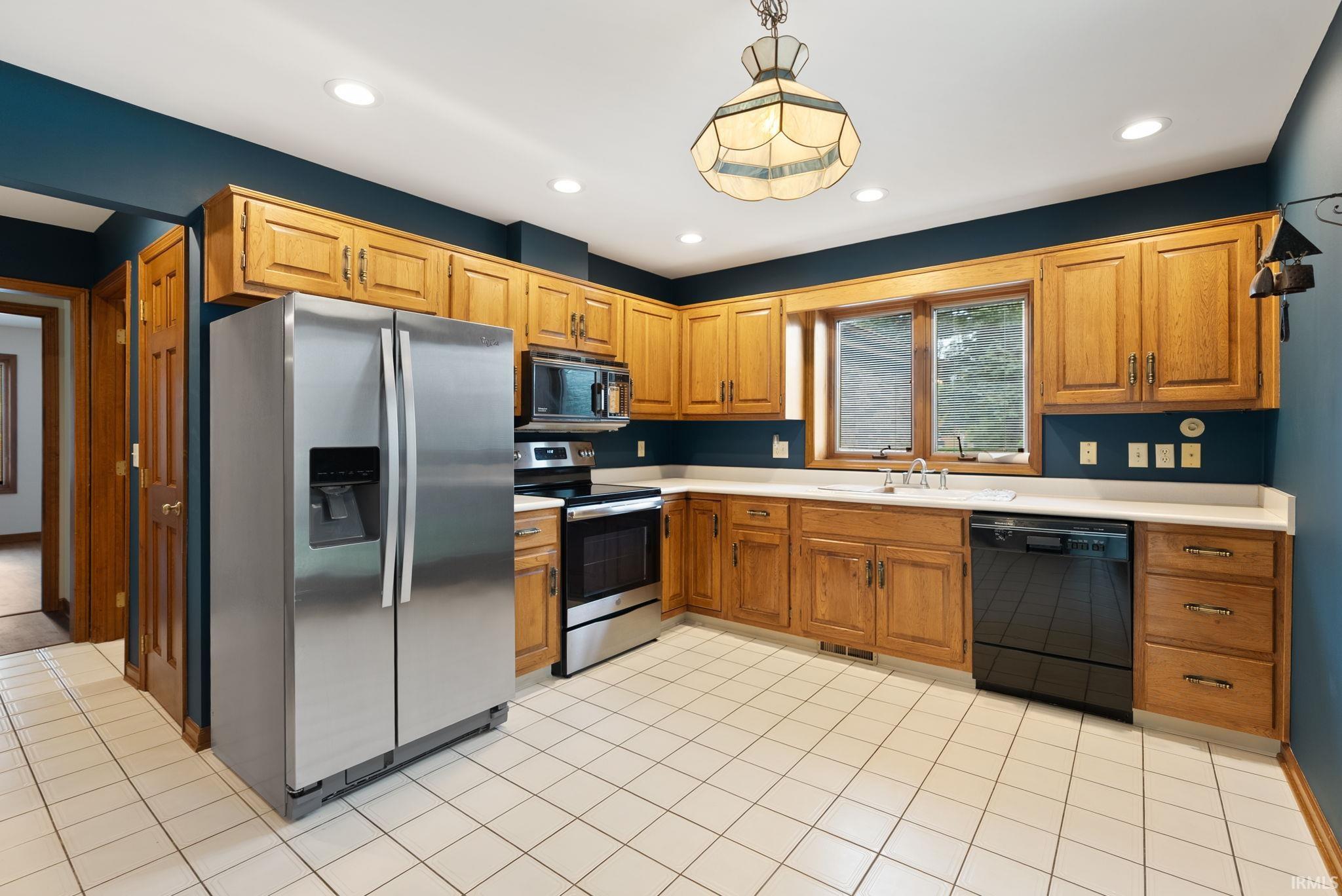Kitchen with black appliances, light countertops, light tile patterned flooring, hanging light fixtures, and wood finish cabinets