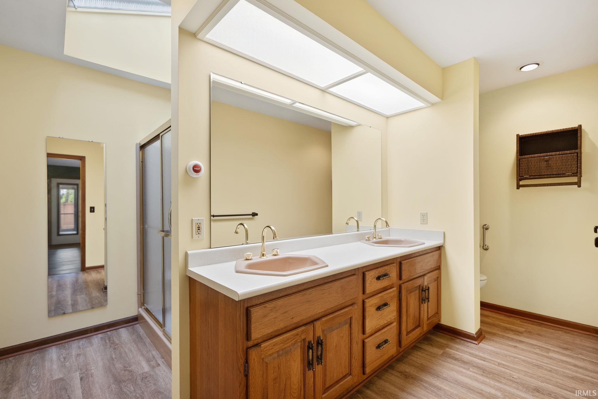 Bathroom featuring double vanity, light wood-style floors, and a shower stall