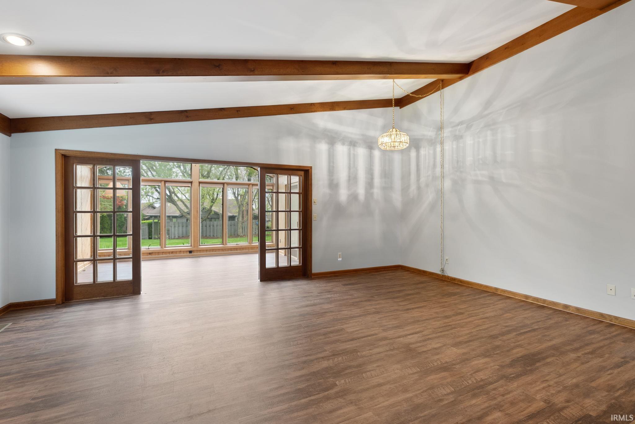Empty room featuring lofted ceiling with beams and dark wood-type flooring