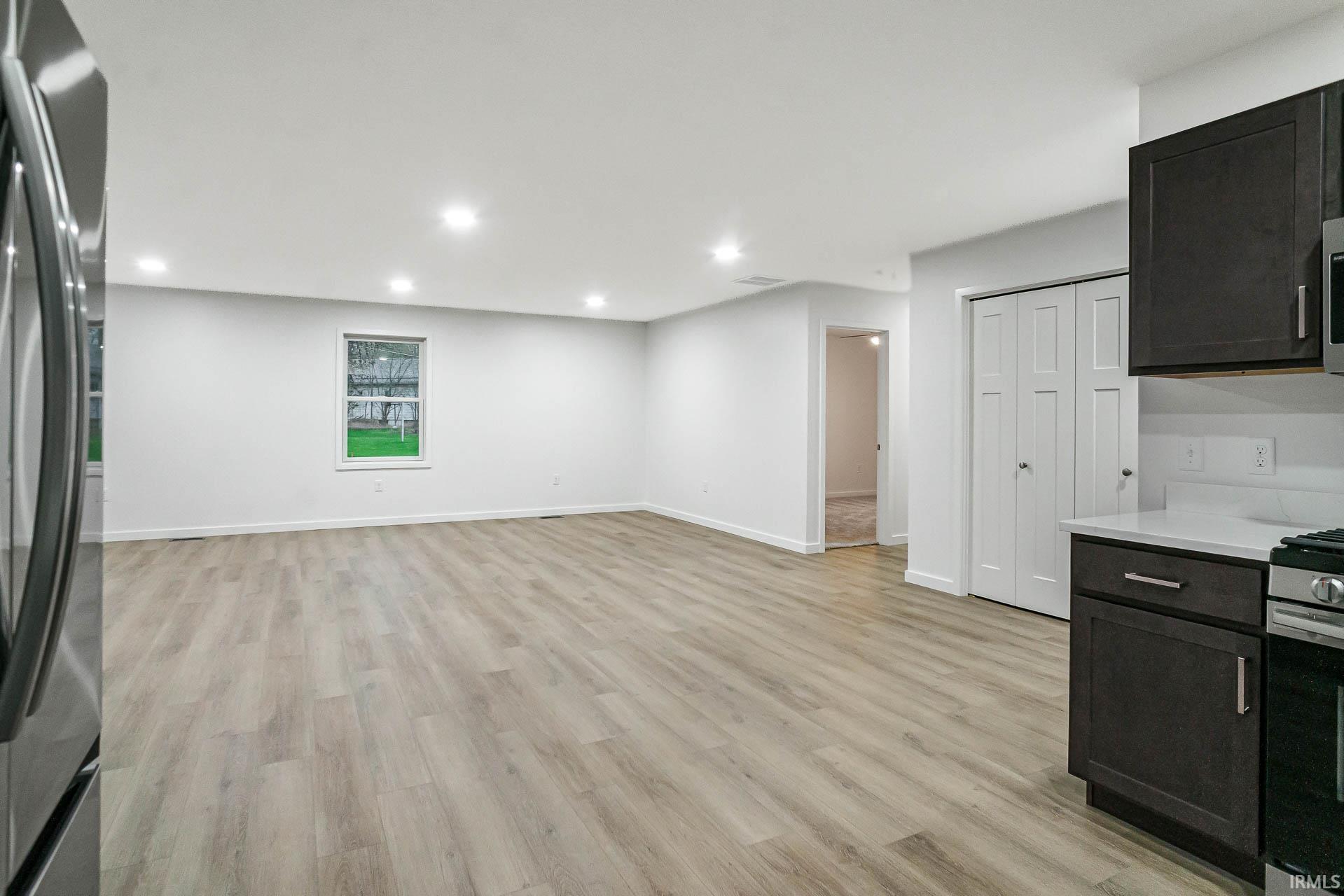 Kitchen with stainless steel appliances, light wood-style flooring, recessed lighting, open floor plan, and light stone countertops