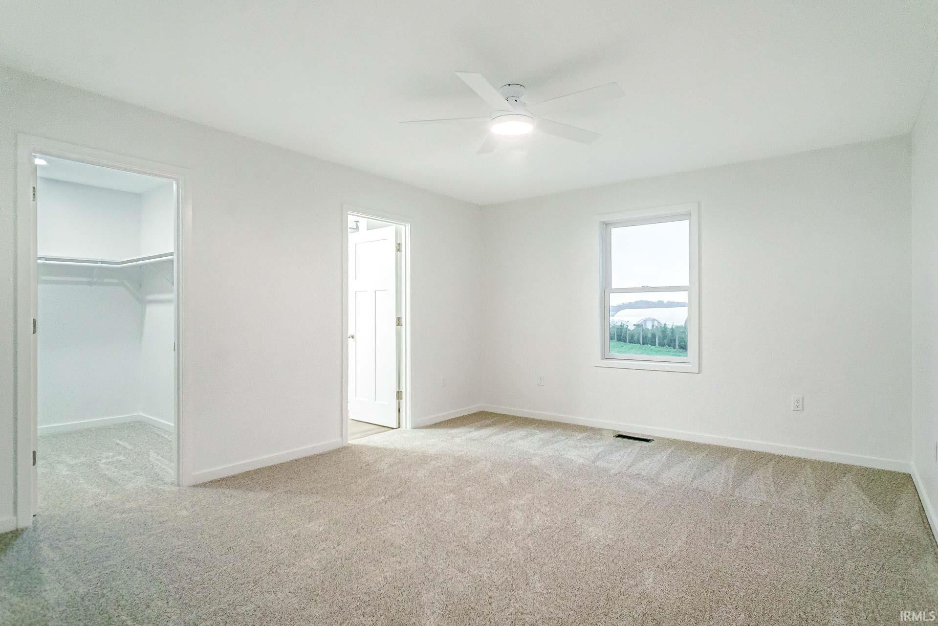 Unfurnished bedroom featuring a spacious closet, light carpet, and a ceiling fan