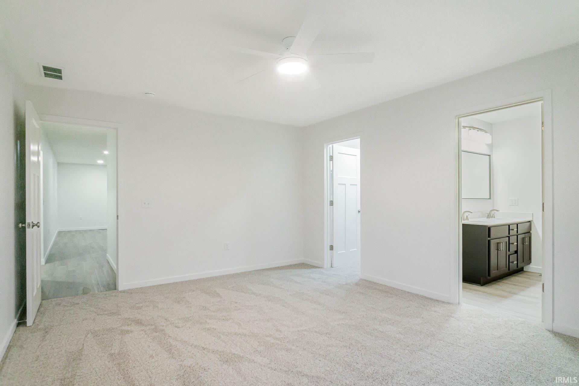 Unfurnished bedroom featuring light colored carpet, a ceiling fan, and ensuite bath