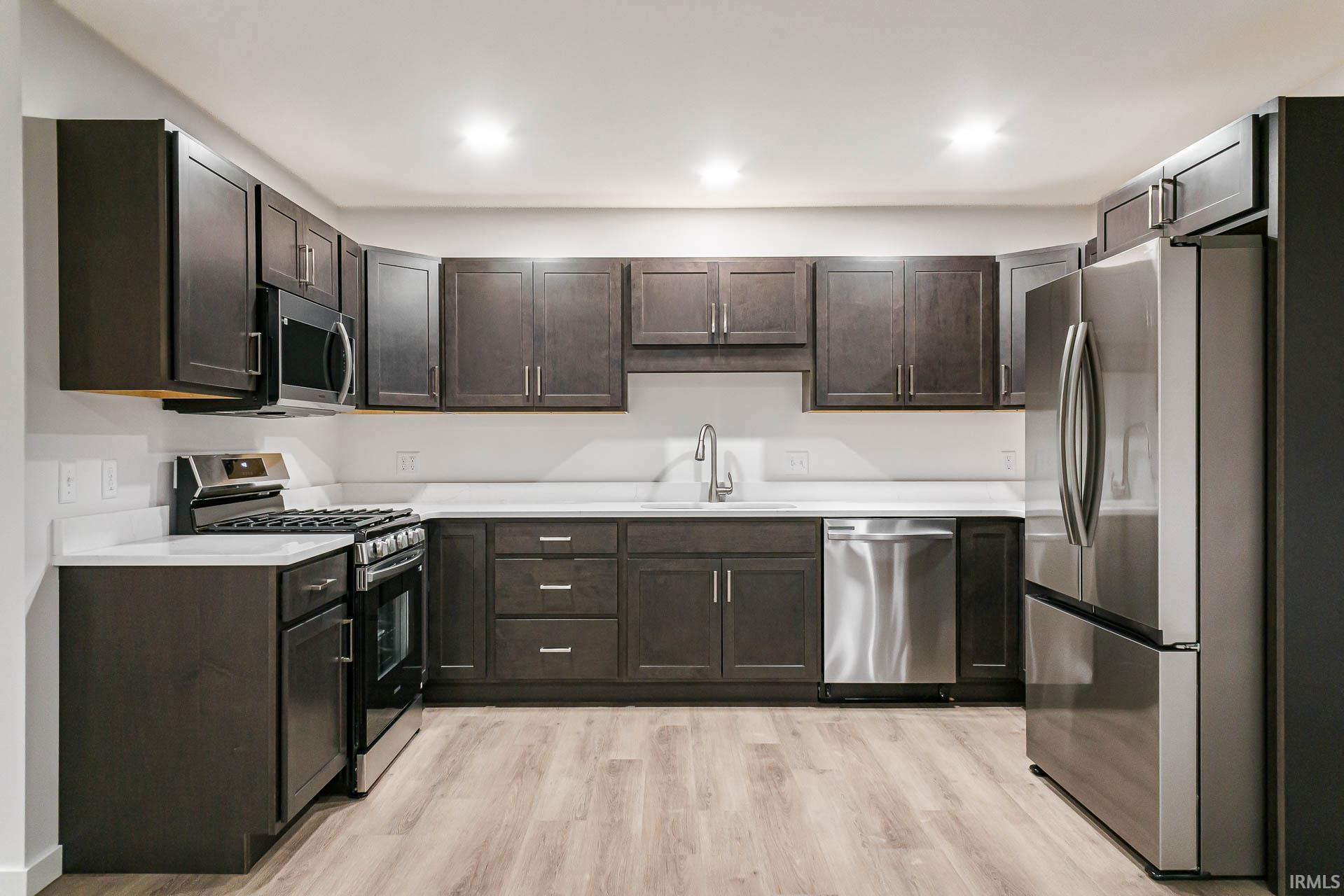 Kitchen featuring stainless steel appliances, dark wood finish cabinets, and light wood-style flooring