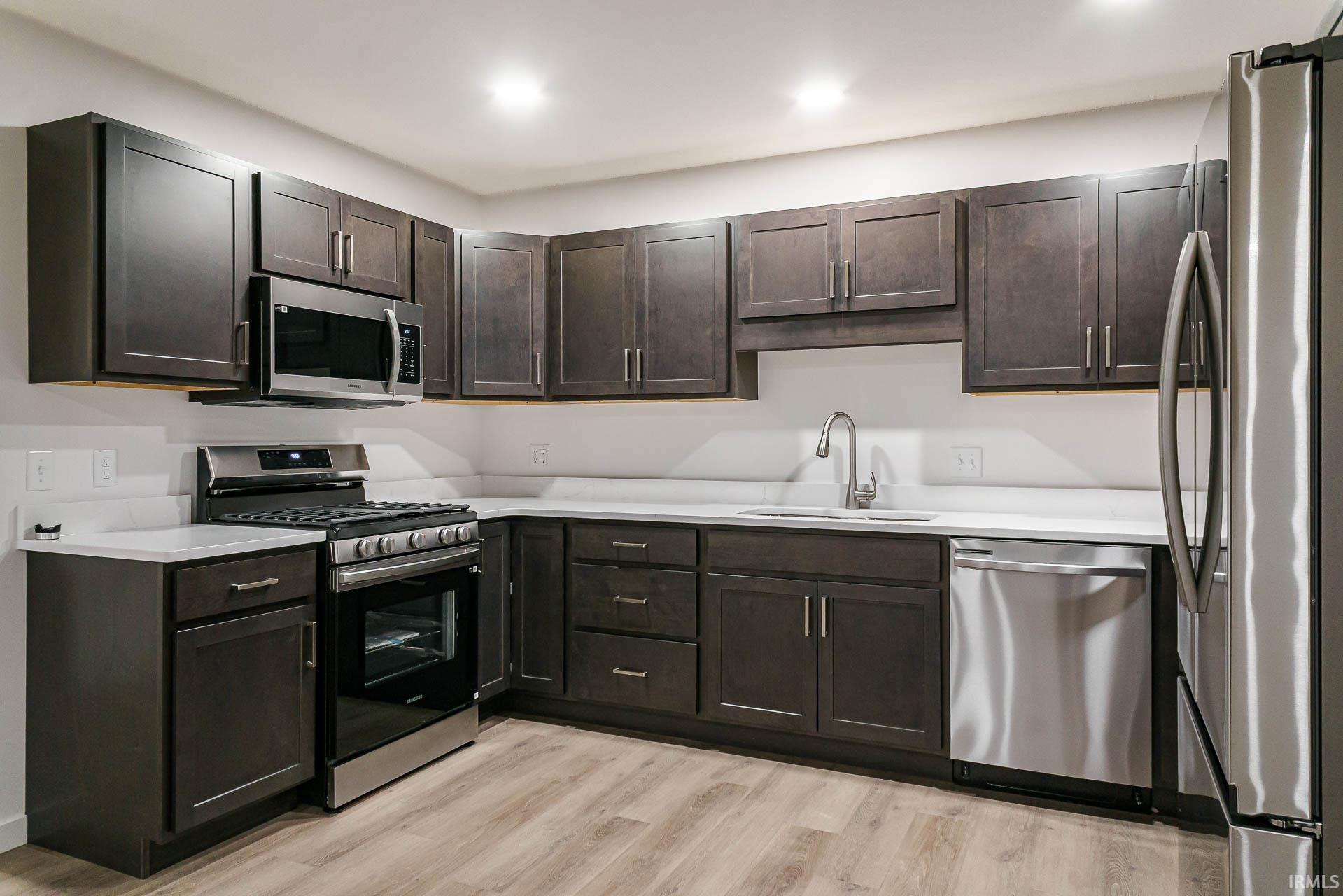Kitchen with stainless steel appliances, light wood finished floors, dark wood finish cabinets, and light stone countertops