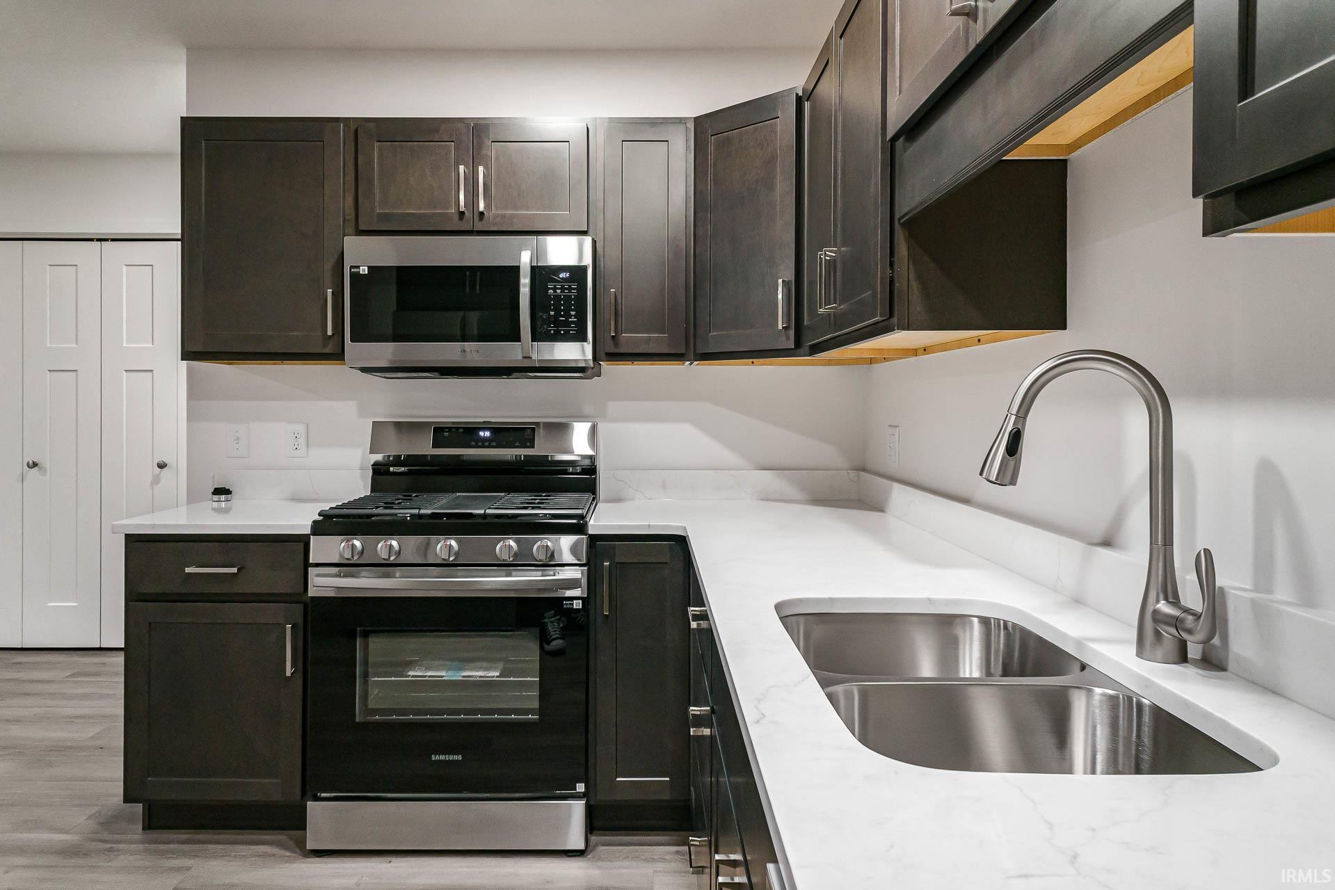 Kitchen with stainless steel appliances, dark wood finish cabinetry, light stone counters, and light wood-style flooring