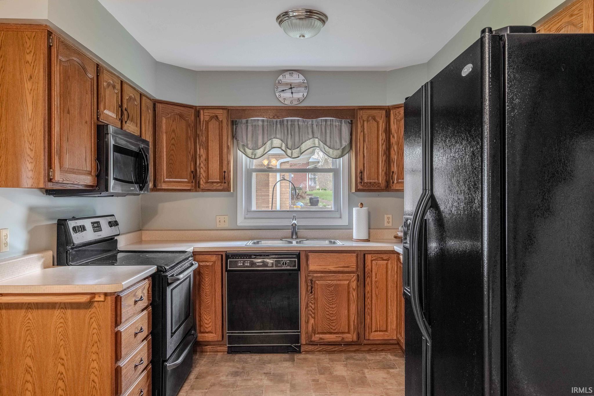 Kitchen featuring black appliances, wood finish cabinets, light countertops, and stone finish floors