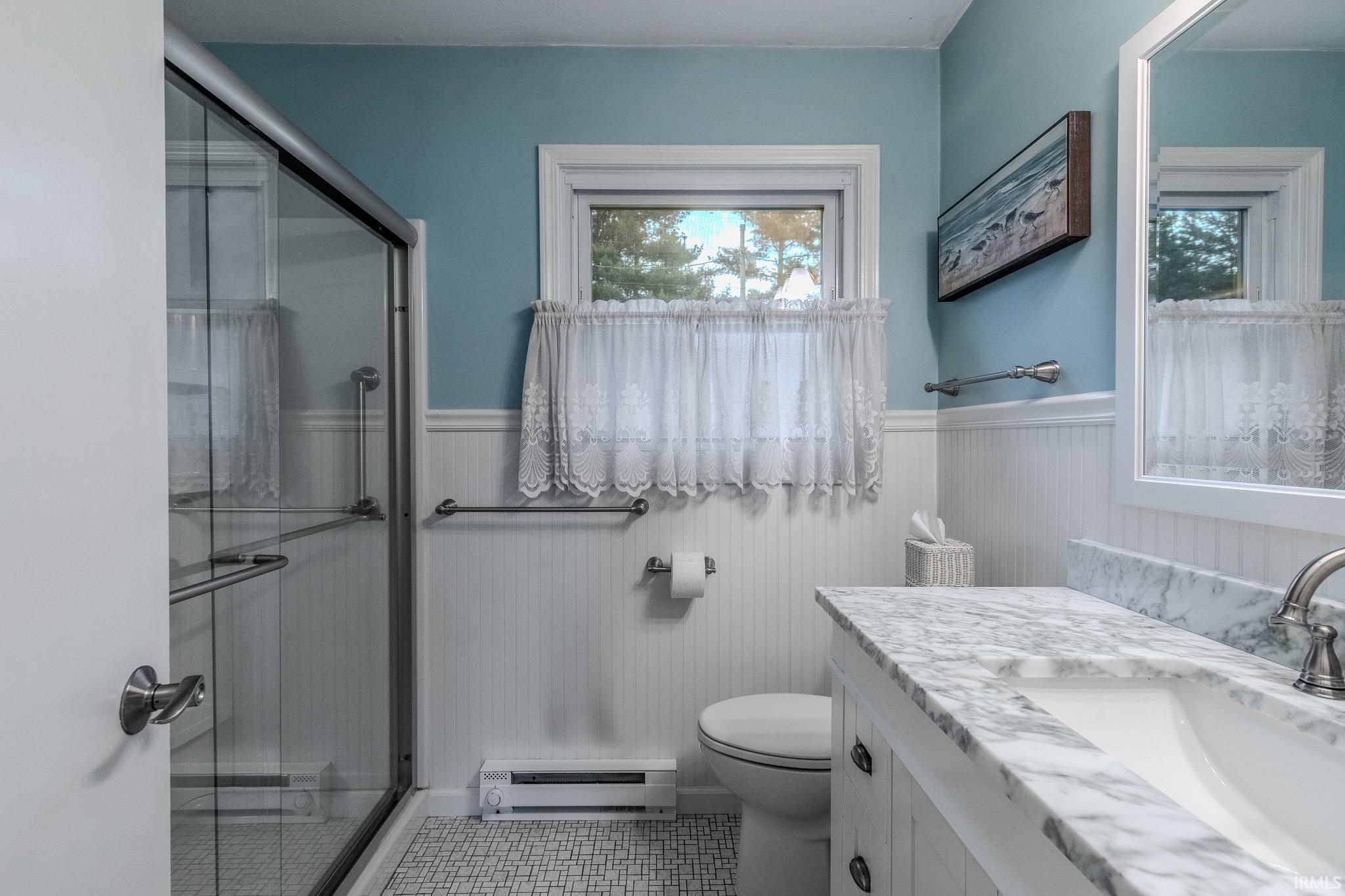 Full bath with a stall shower, vanity, baseboard heating, a wainscoted wall, and a baseboard radiator