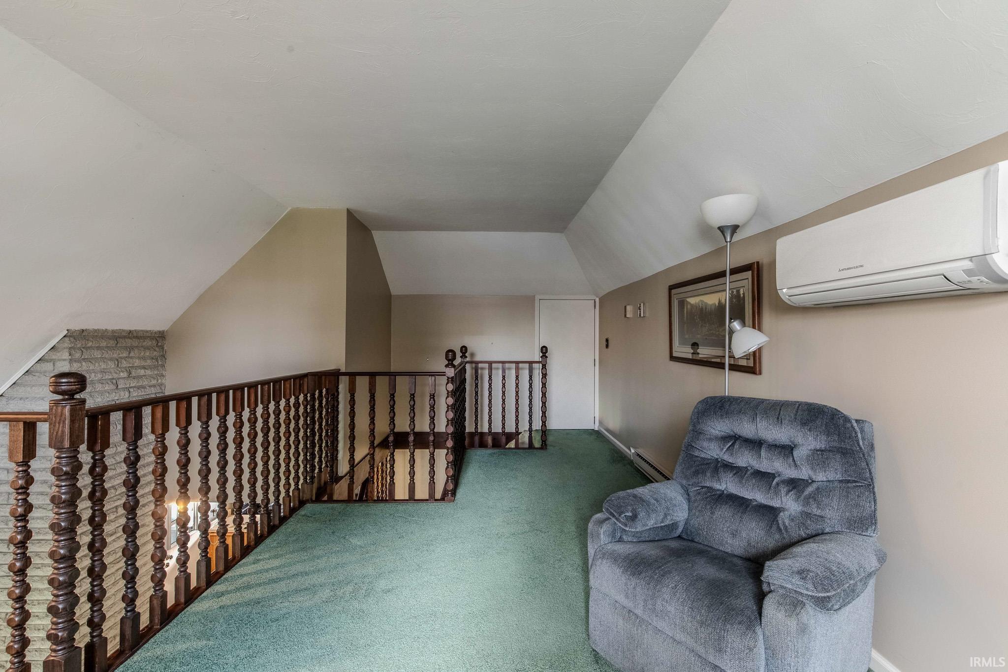 Living area featuring carpet floors, vaulted ceiling, a baseboard heating unit, and an upstairs landing