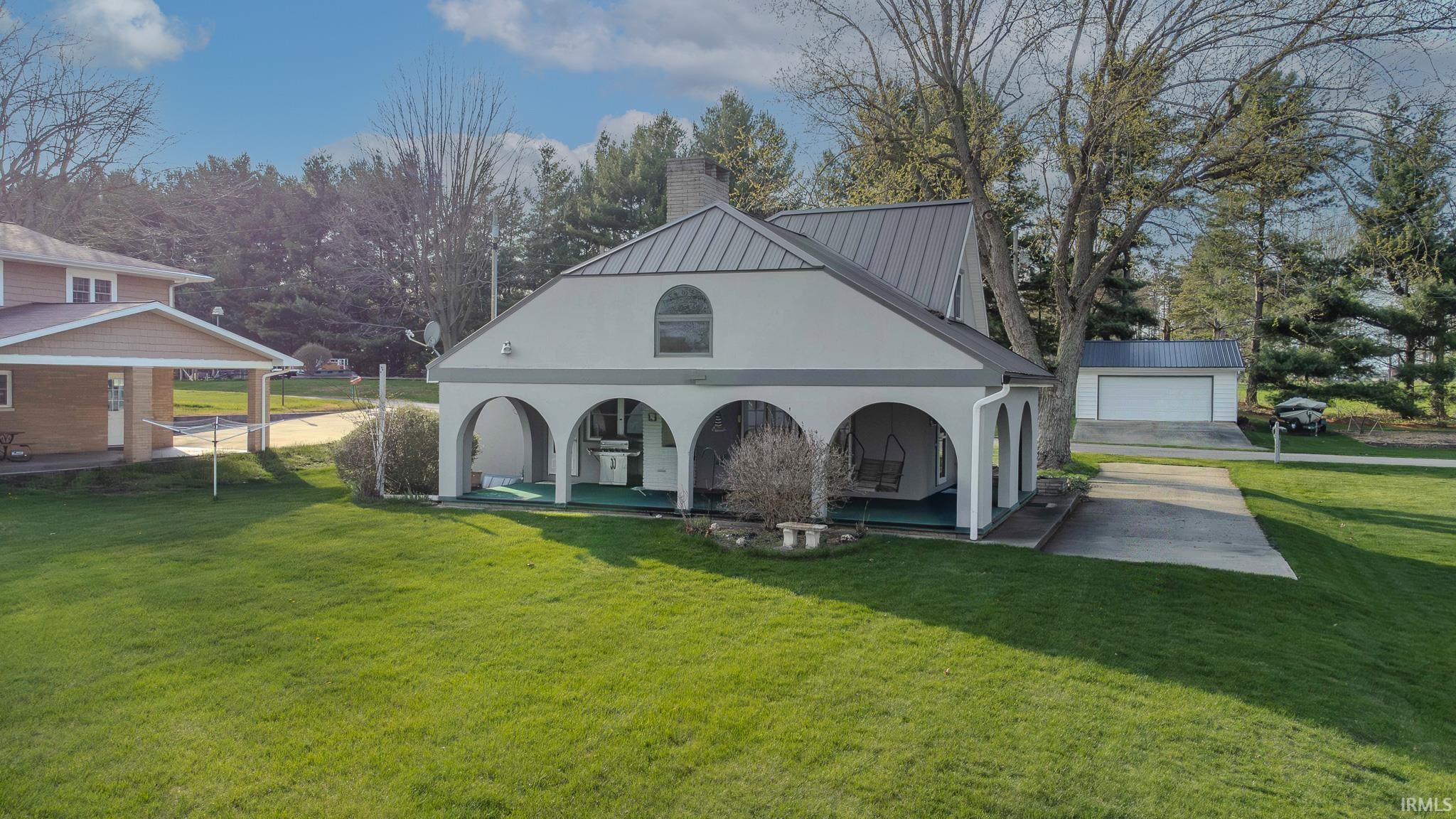 Back of house with stucco siding, a chimney, a lawn, covered porch, and a metal roof