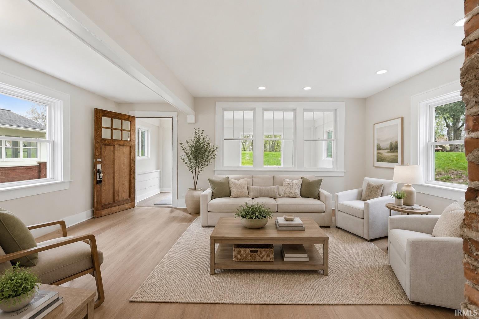 Living area featuring wood-finish flooring, ample natural light from multiple windows, and a classic wood entry door