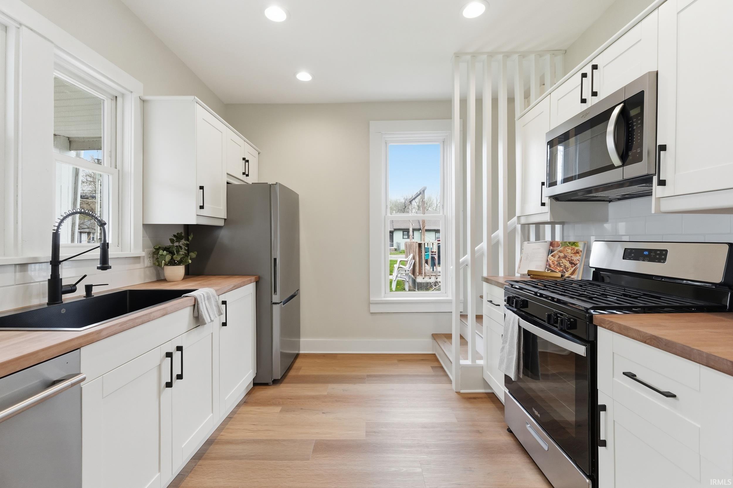 Kitchen with stainless steel appliances, butcher block counters, tasteful backsplash, white cabinets, and recessed lighting