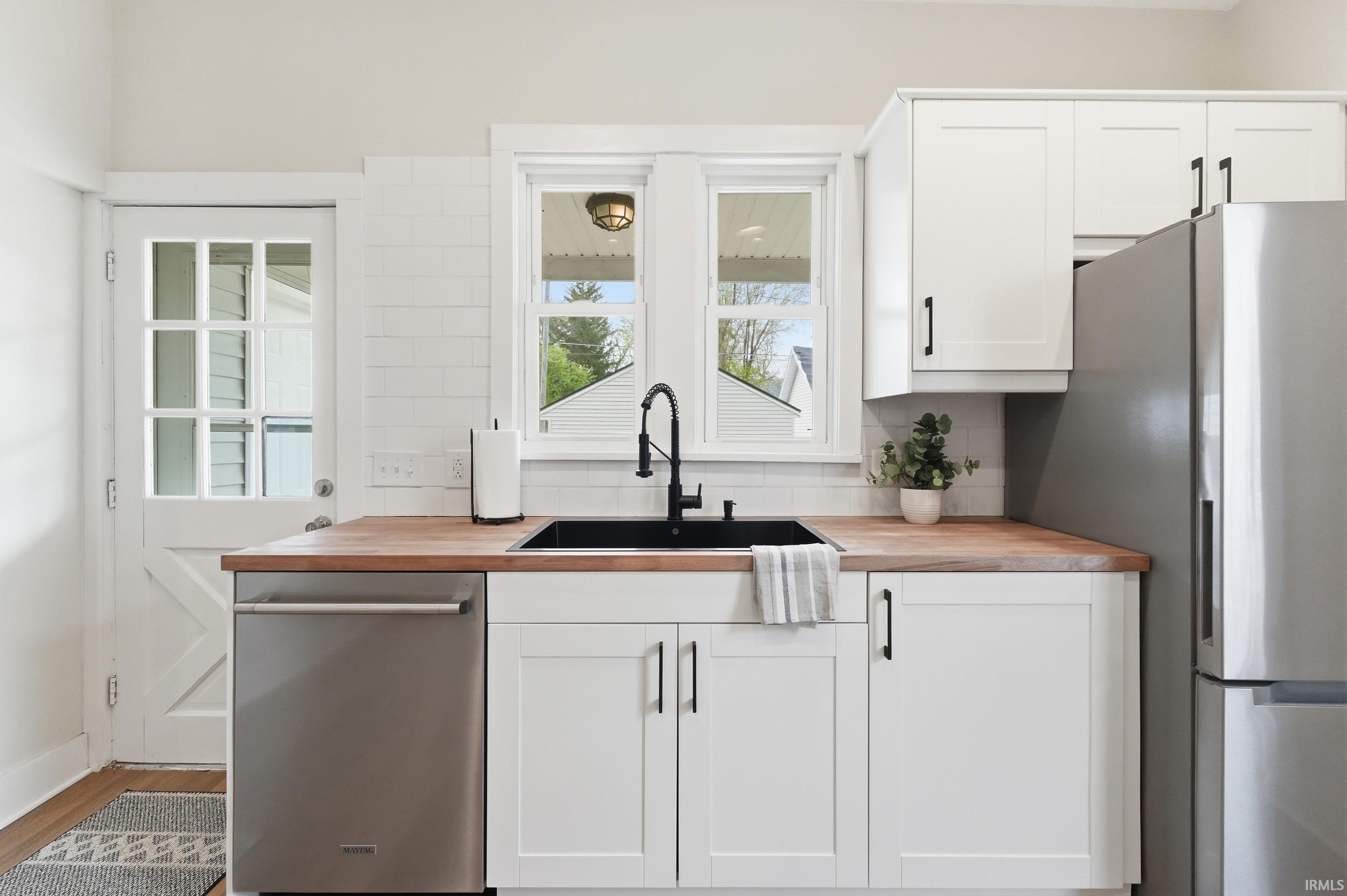 Kitchen with wooden counters, white cabinets, stainless steel appliances, and light wood-style flooring