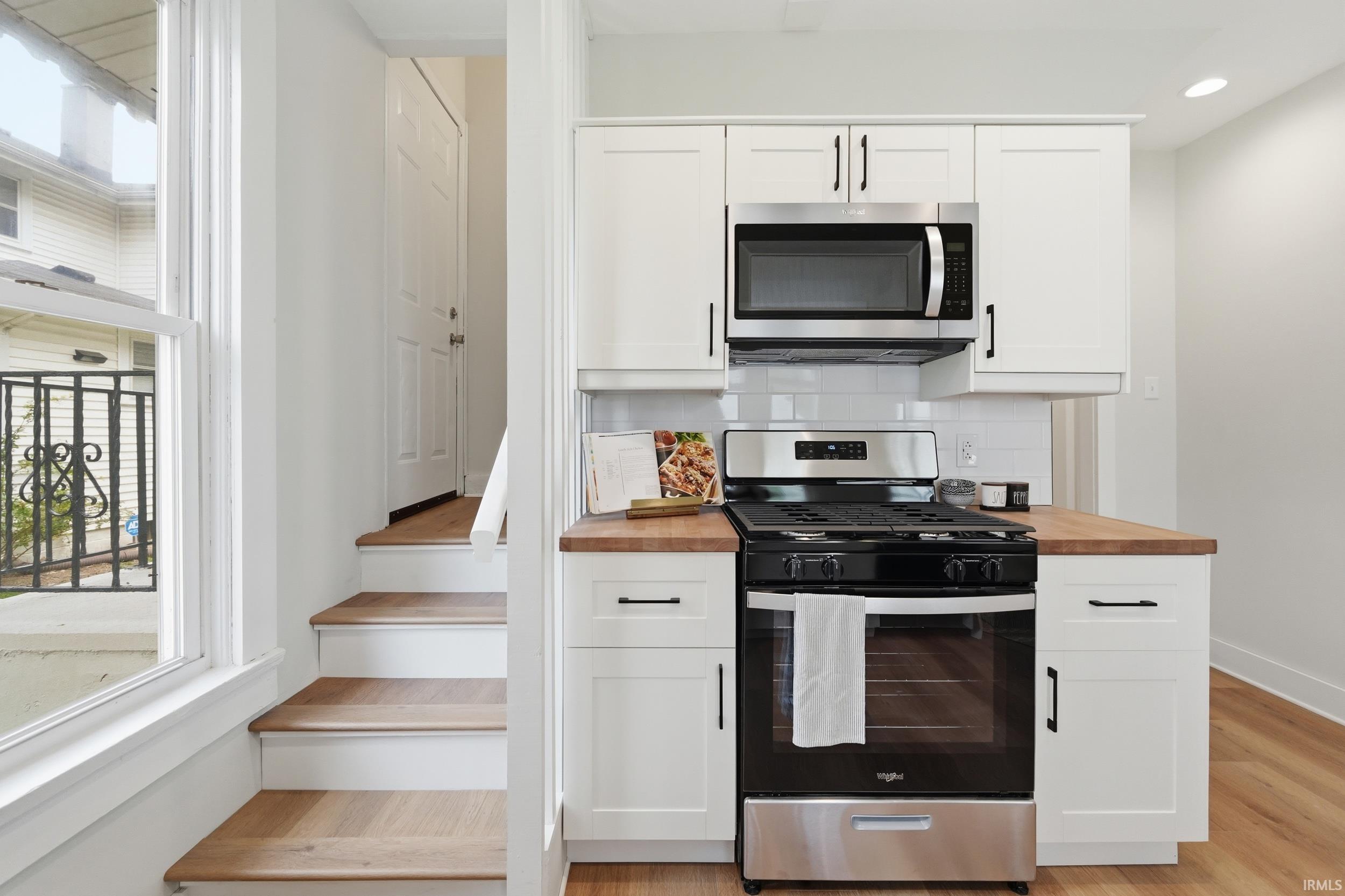 Kitchen with stainless steel appliances, white cabinetry, backsplash, and light wood-type flooring