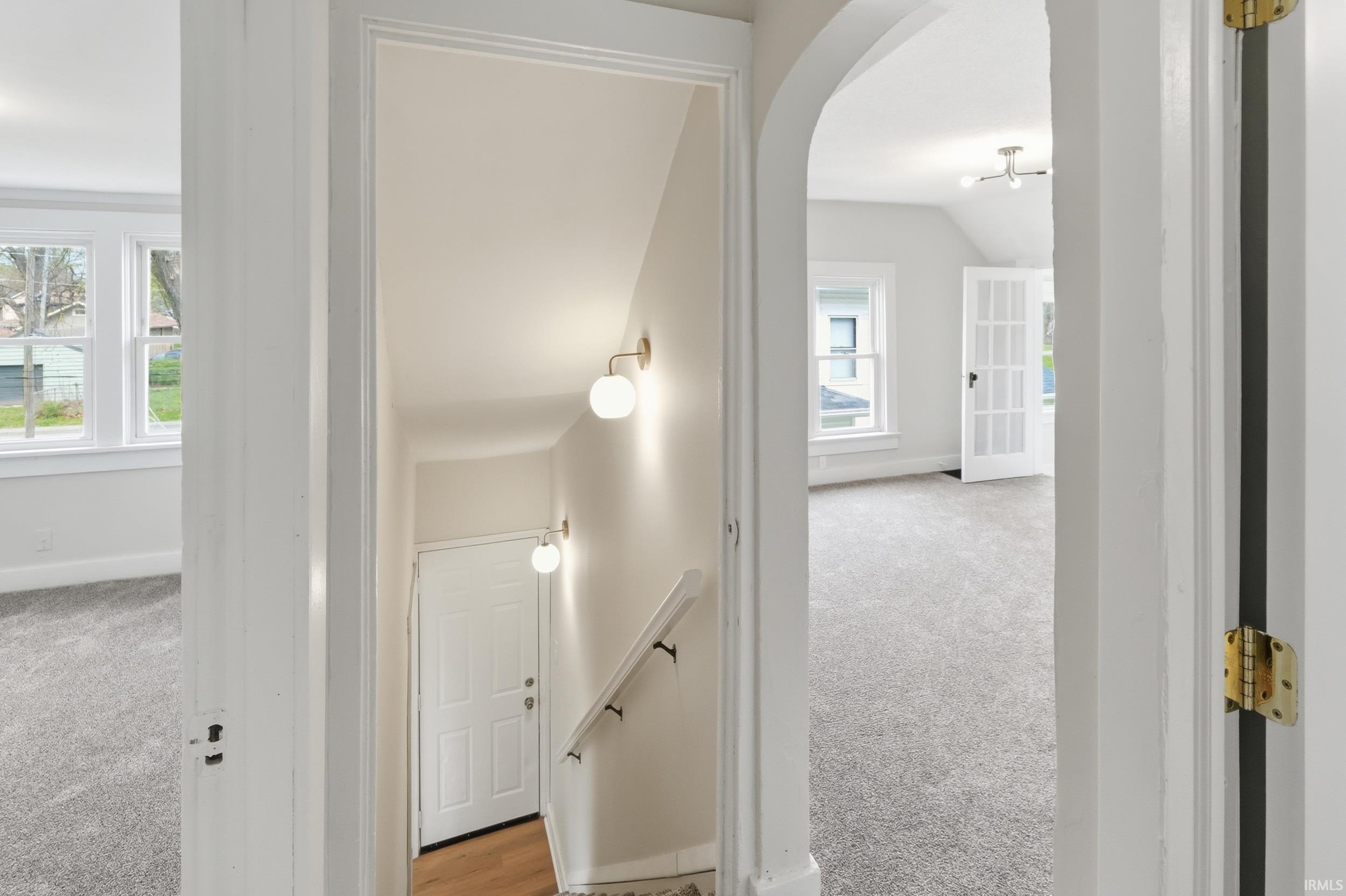 Hallway featuring light colored carpet, arched walkways, and an upstairs landing