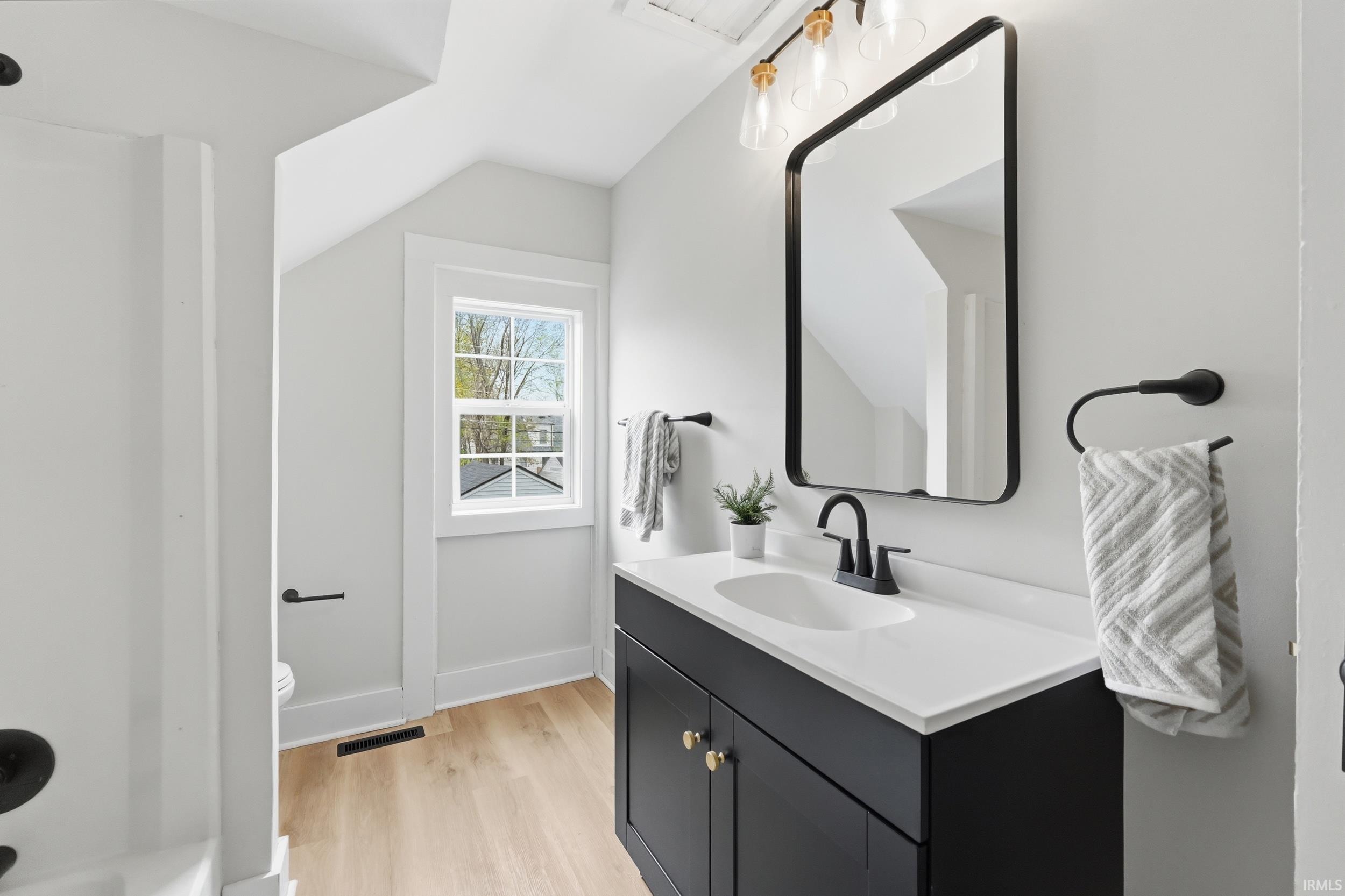 Full bathroom featuring vanity, vaulted ceiling, and light wood-type flooring