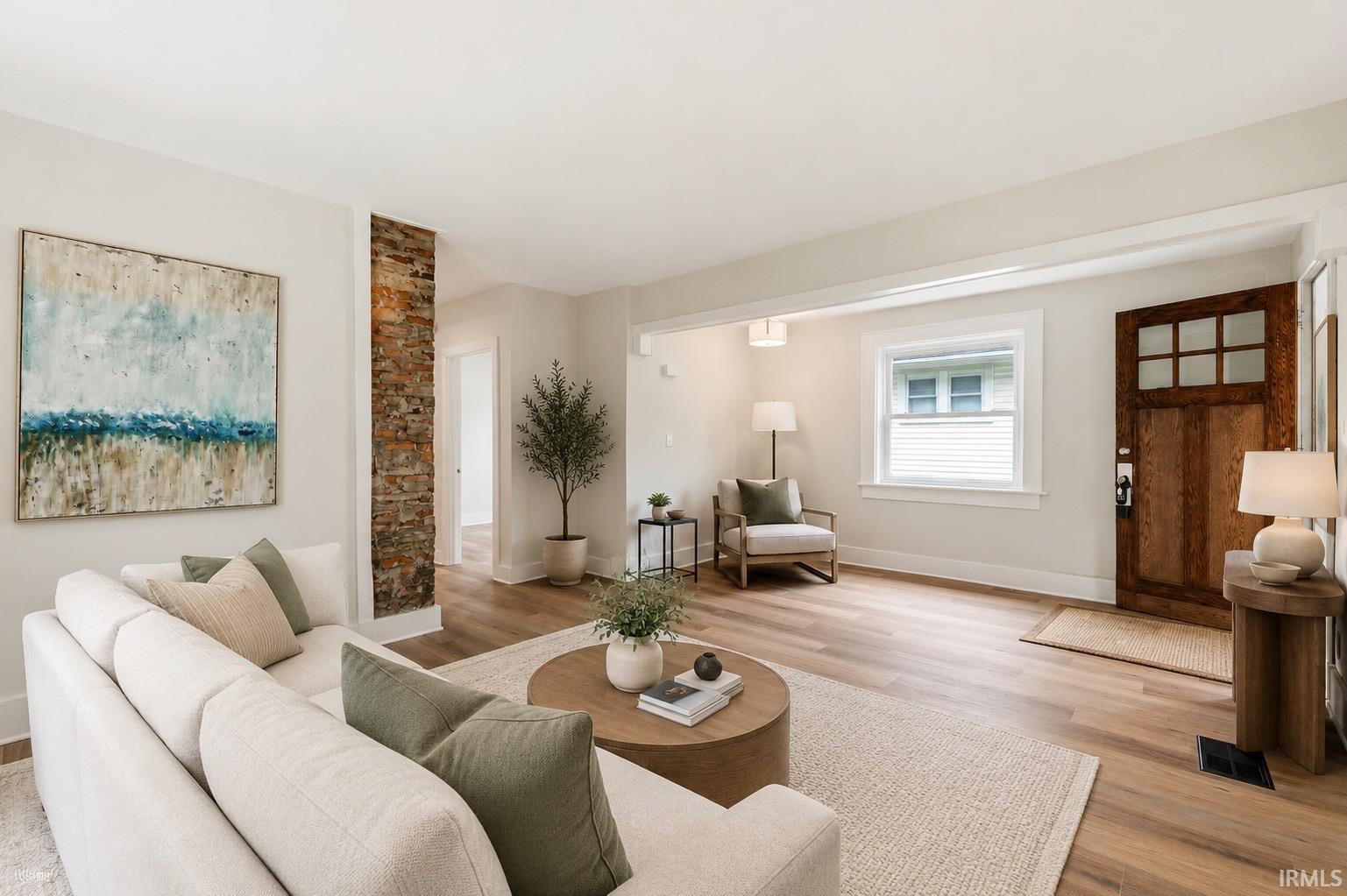 Open-concept living space featuring wood-finish flooring, a decorative exposed brick column, and white window trim