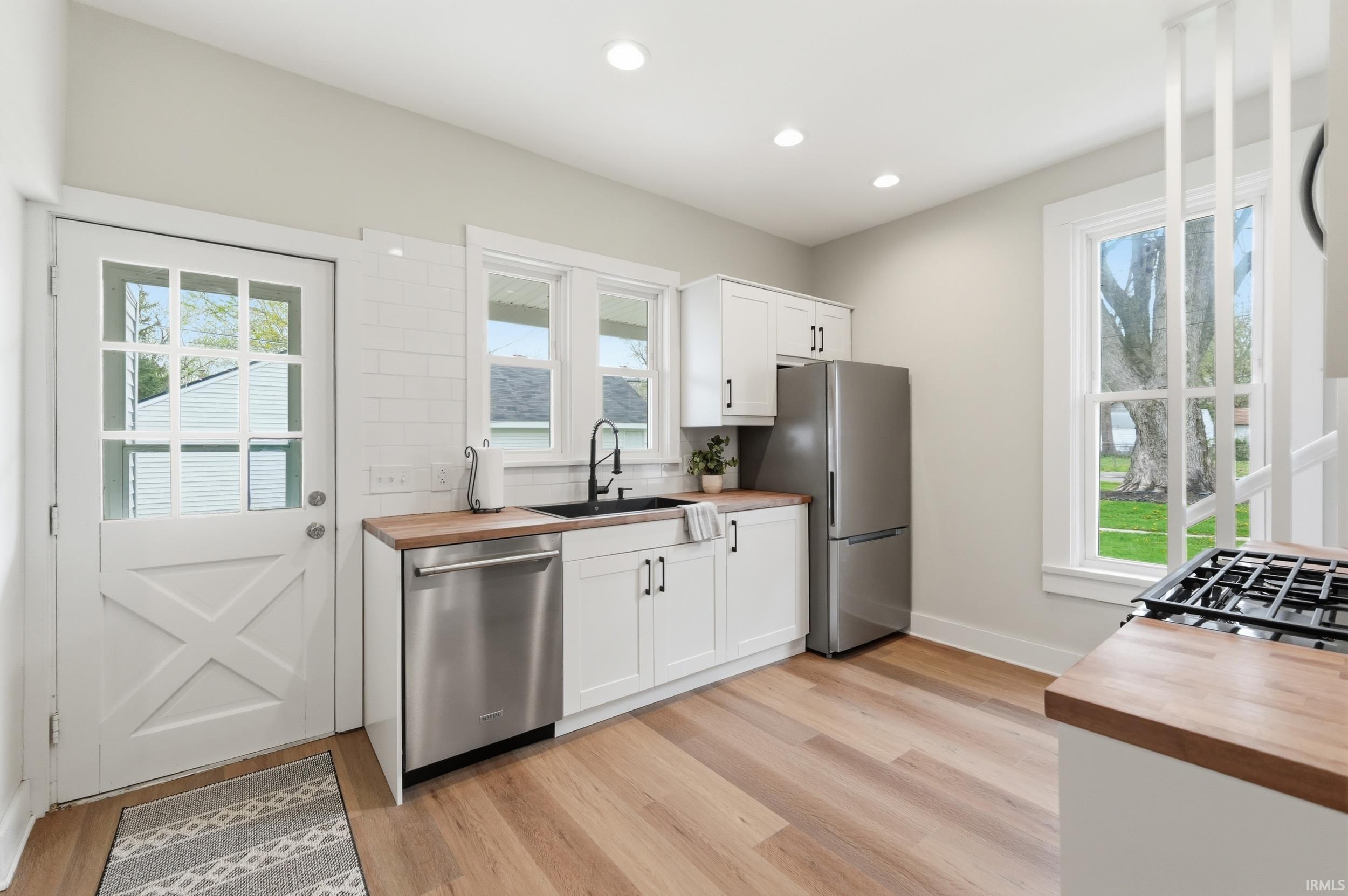 Kitchen with wooden counters, stainless steel appliances, white cabinets, light wood-type flooring, and recessed lighting