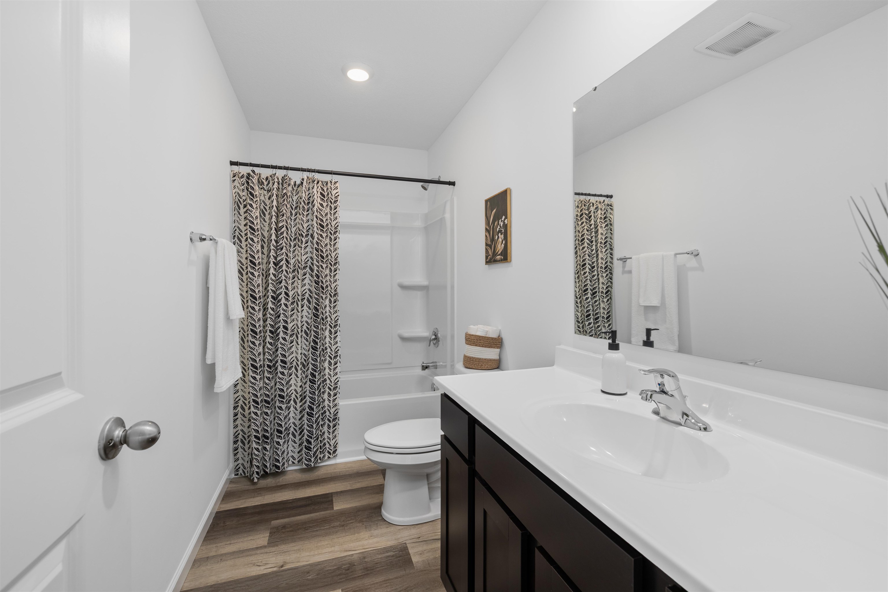 Full bathroom featuring a single vanity with a white countertop and integrated sink, a dark wood-finish cabinet, and a large wall-mounted mirror
