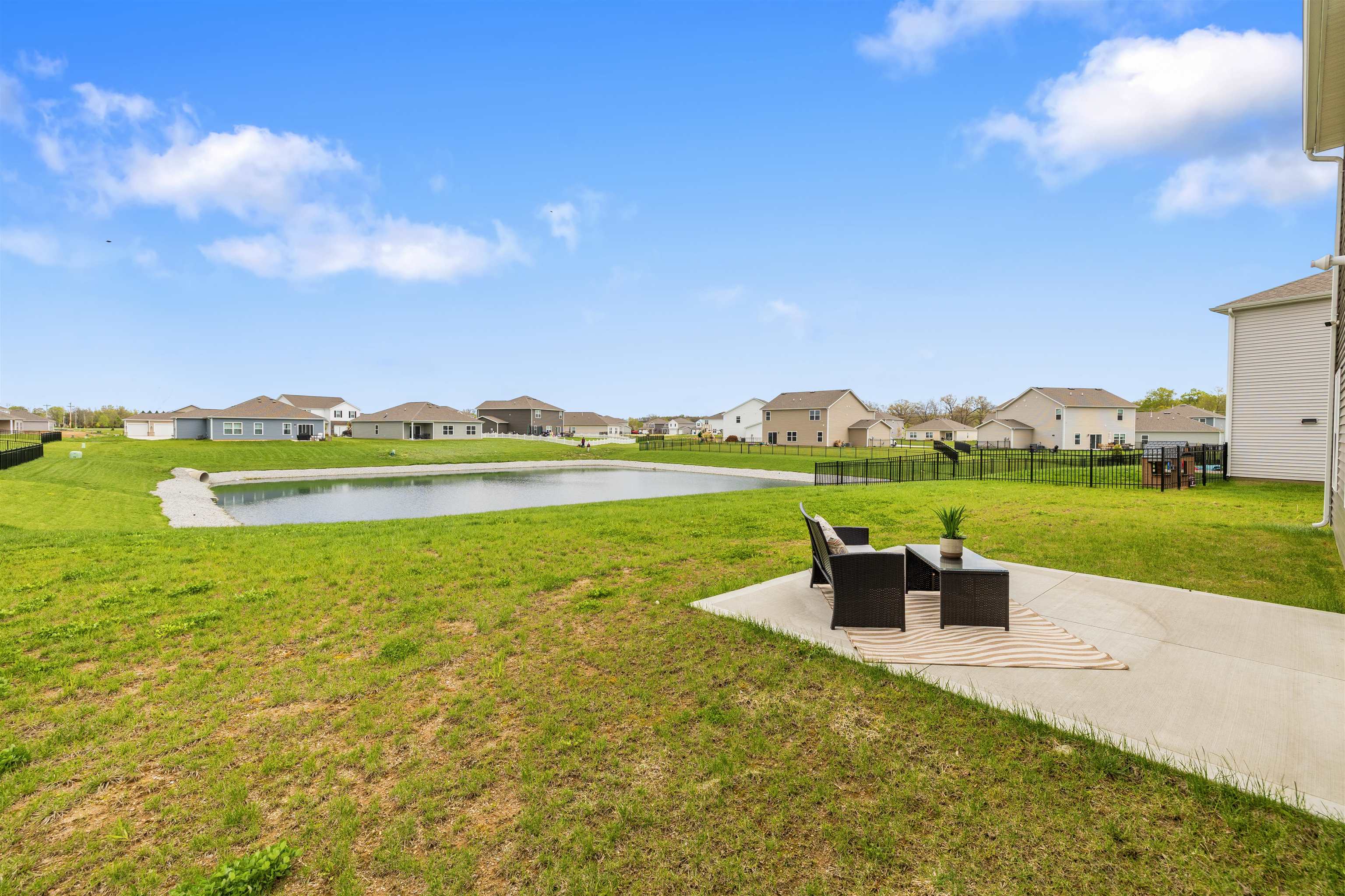 Expansive backyard featuring a concrete patio, green lawn, and a retention pond