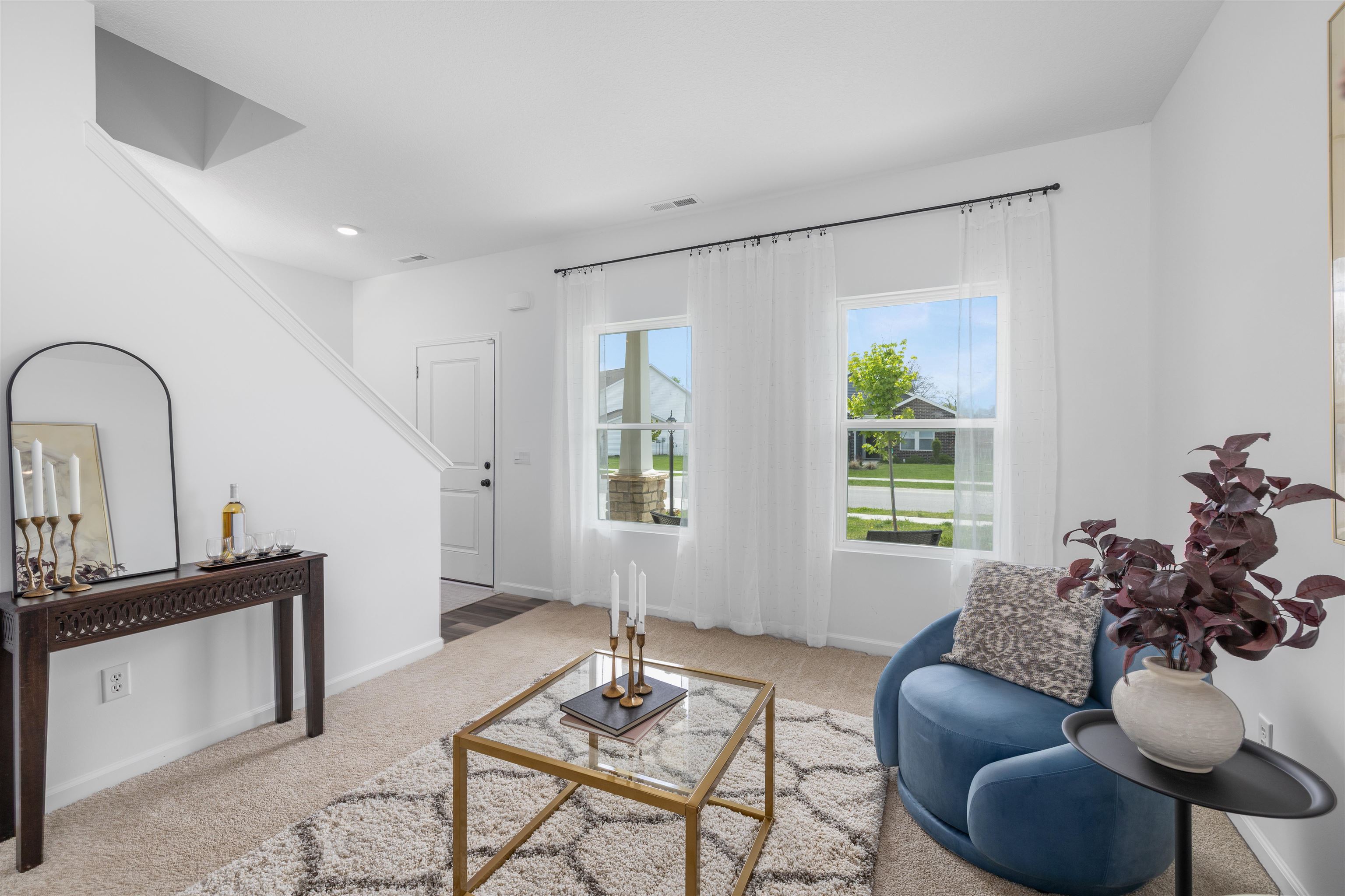 Bright living area featuring twin windows with white sheer curtains, a neutral carpet, and a staircase with white risers and stringers