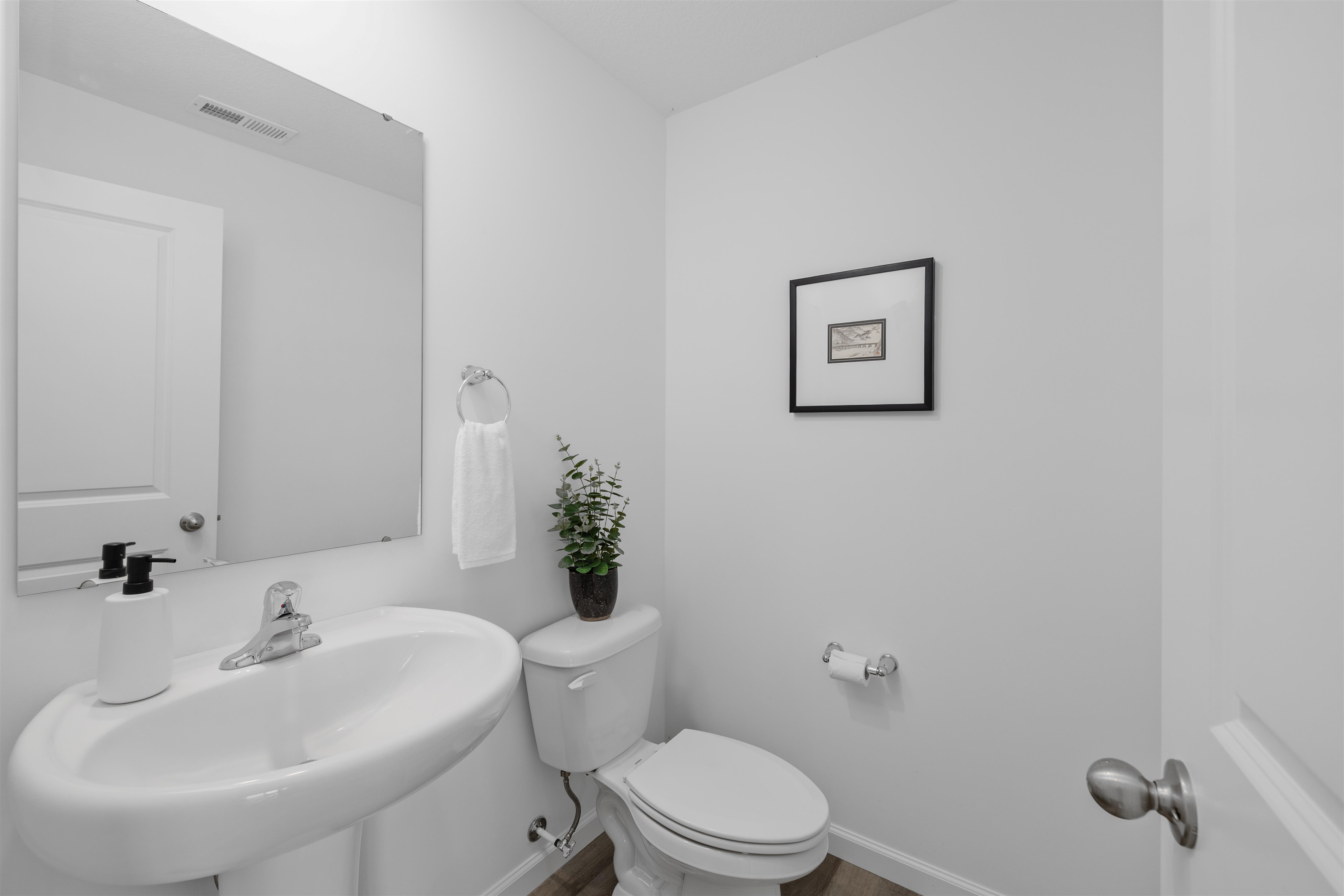 White pedestal sink with chrome faucet, large frameless mirror, and wood-finish flooring