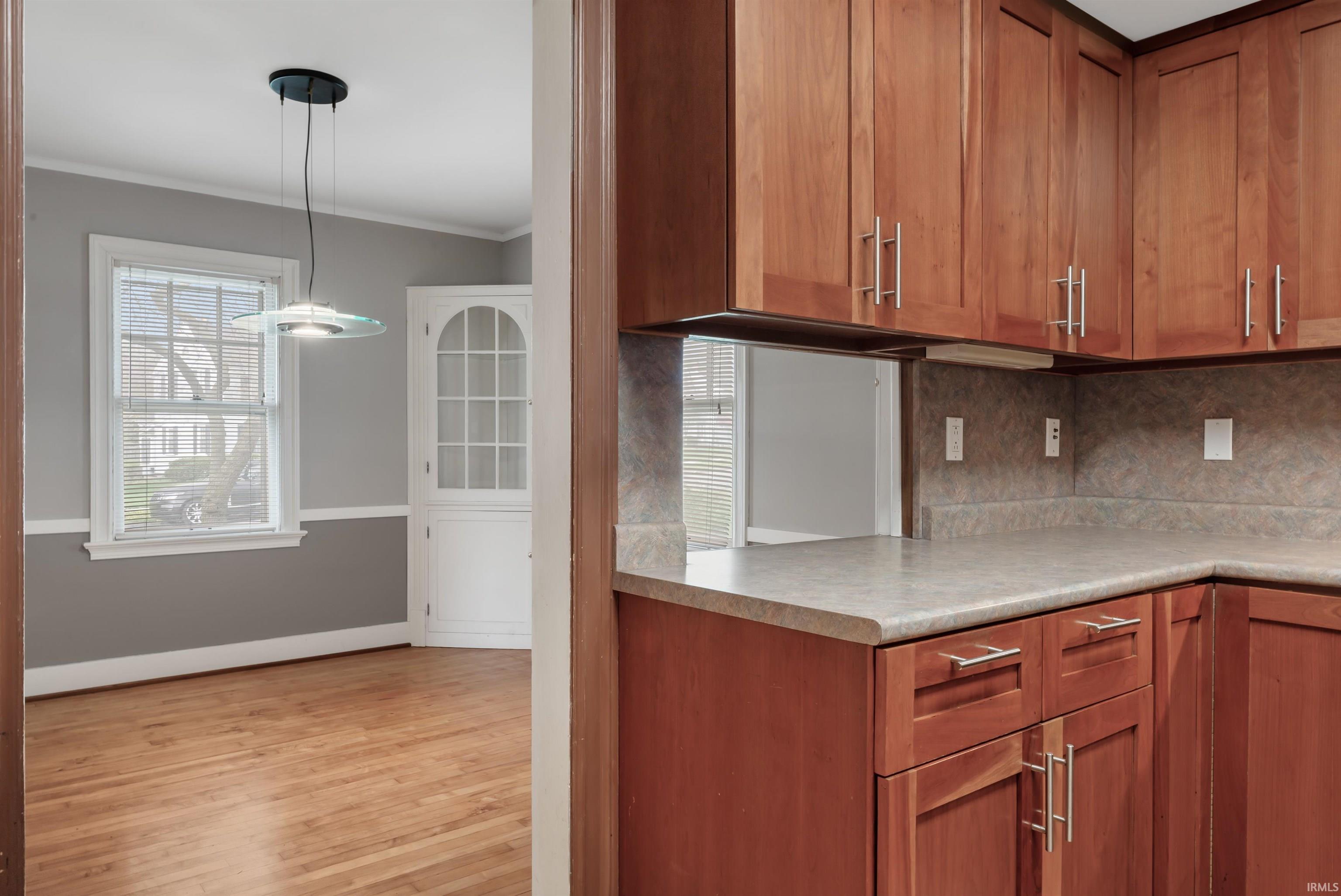 Kitchen with ornamental molding, wood finish cabinets, light countertops, light wood-style floors, and tasteful backsplash