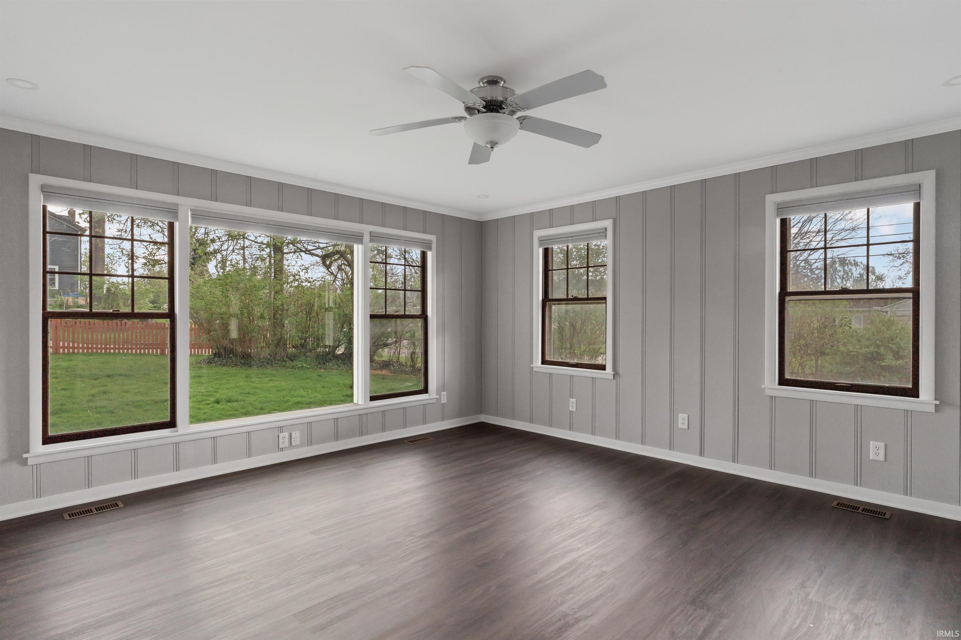 Empty room featuring a ceiling fan, dark wood-style flooring, plenty of natural light, a decorative wall, and crown molding