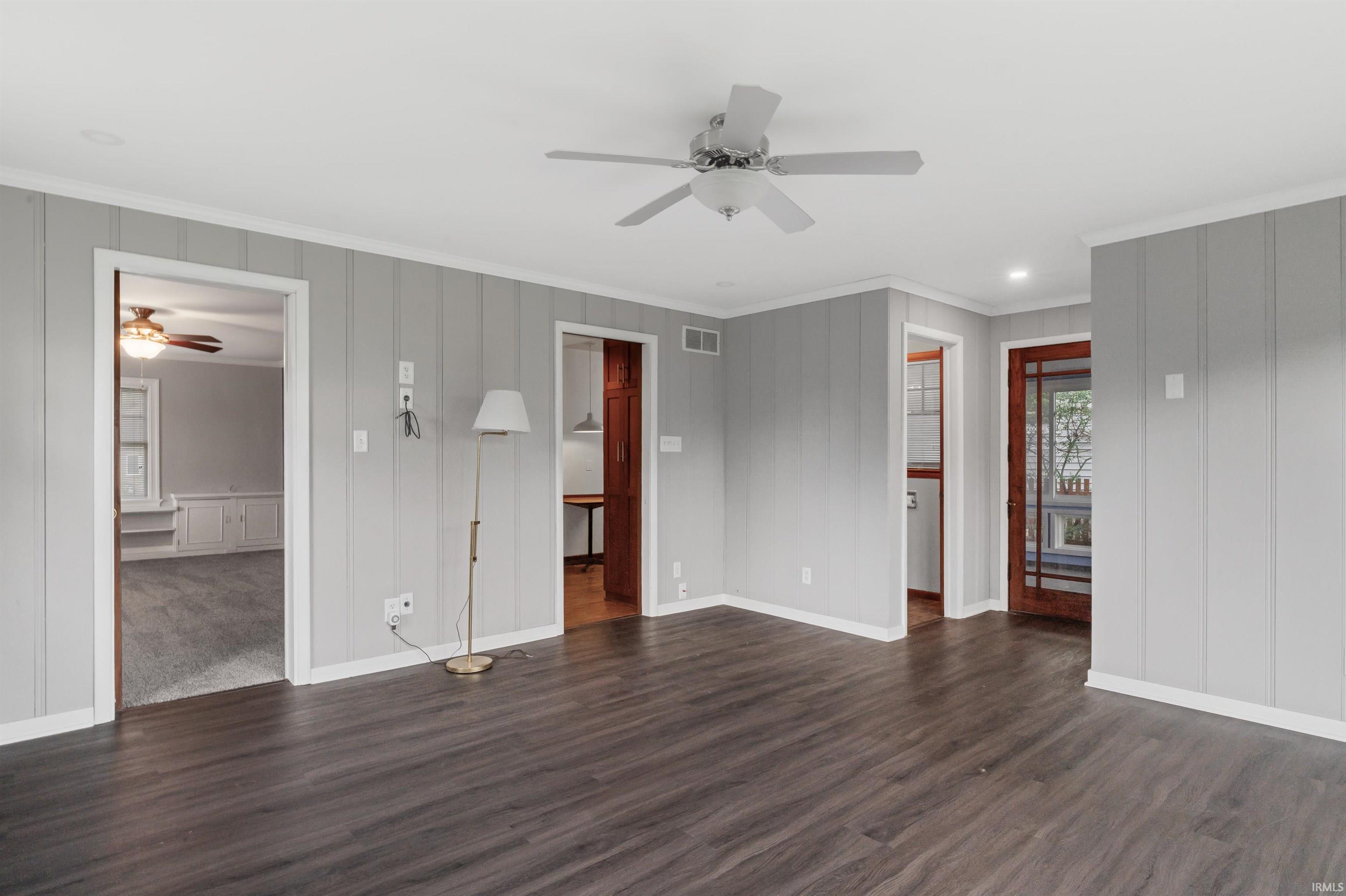 Unfurnished living room featuring a ceiling fan, dark wood-style flooring, and crown molding