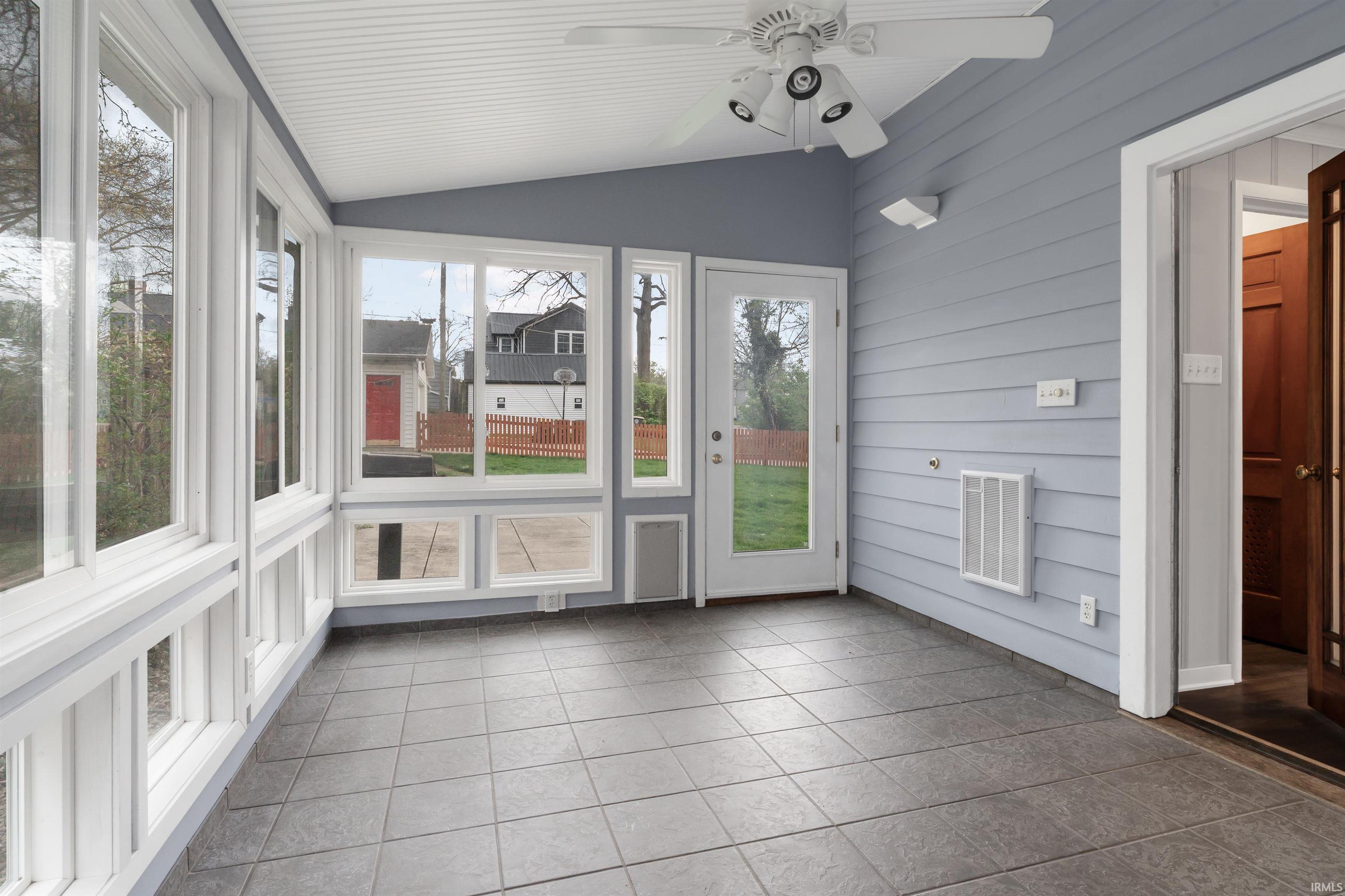 Unfurnished sunroom with tile patterned floors, lofted ceiling, and wood walls