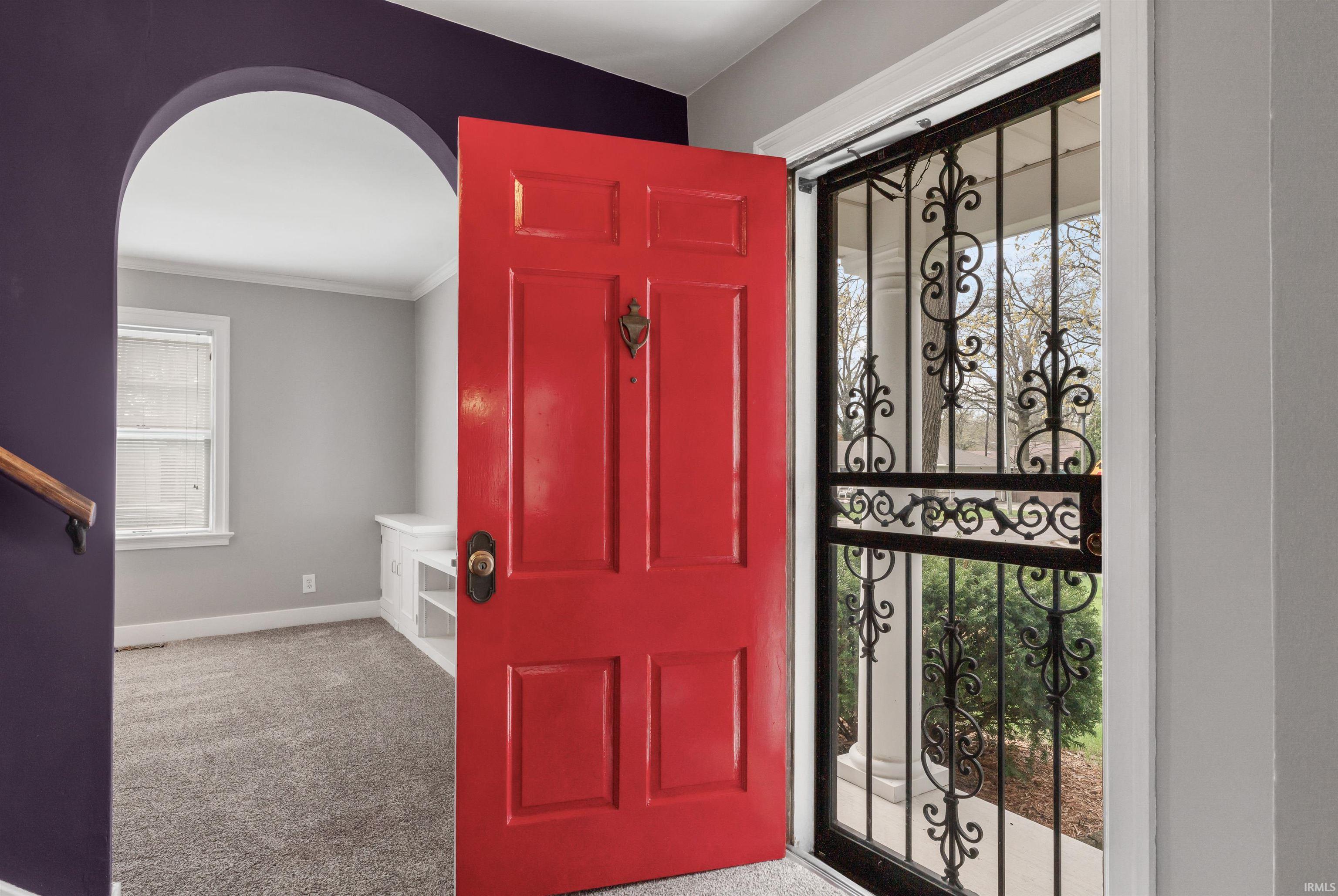 Foyer entrance with light colored carpet, arched walkways, and crown molding
