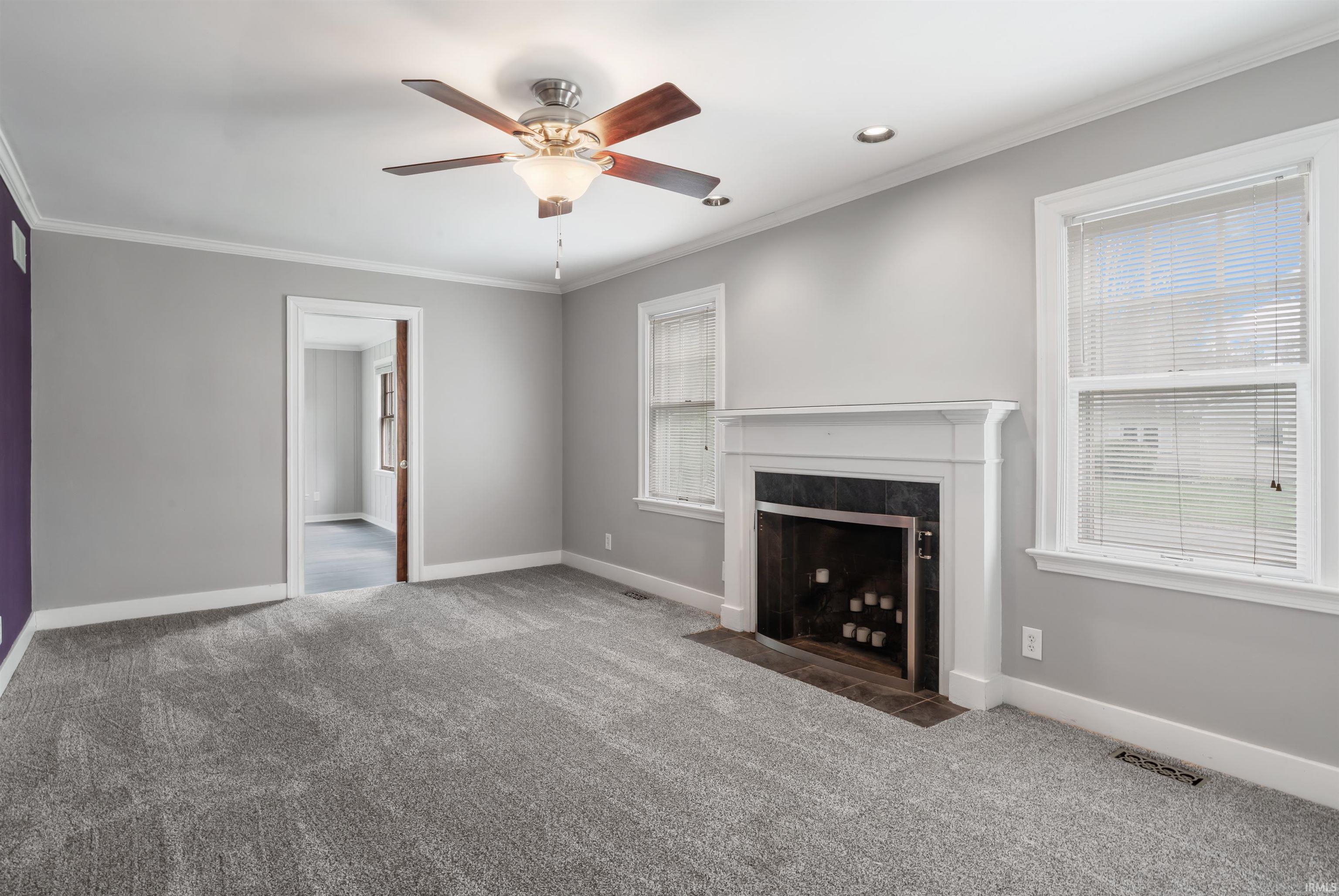 Unfurnished living room featuring crown molding, carpet flooring, ceiling fan, and a fireplace with flush hearth