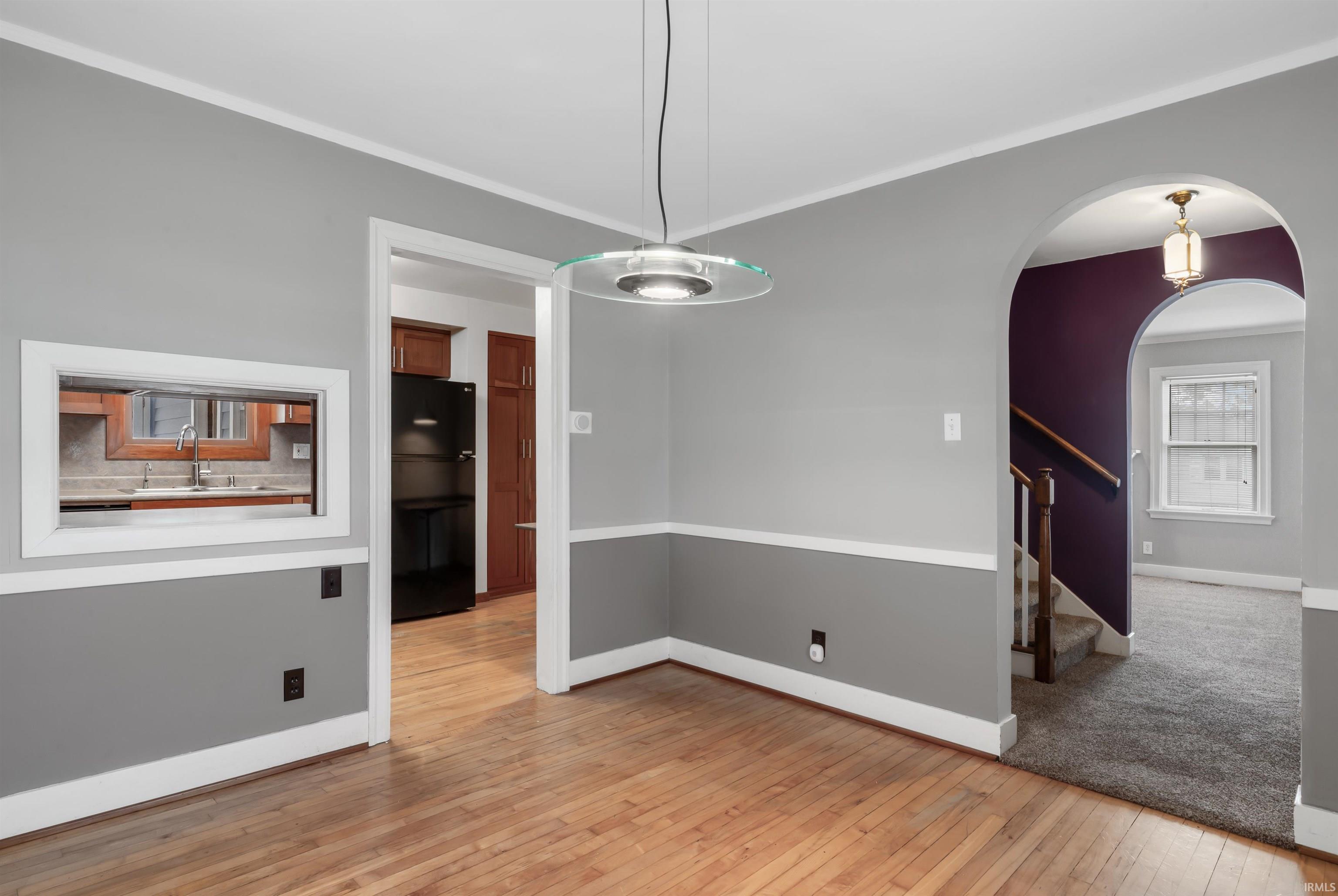 Unfurnished dining area featuring light wood-style flooring, crown molding, and arched walkways