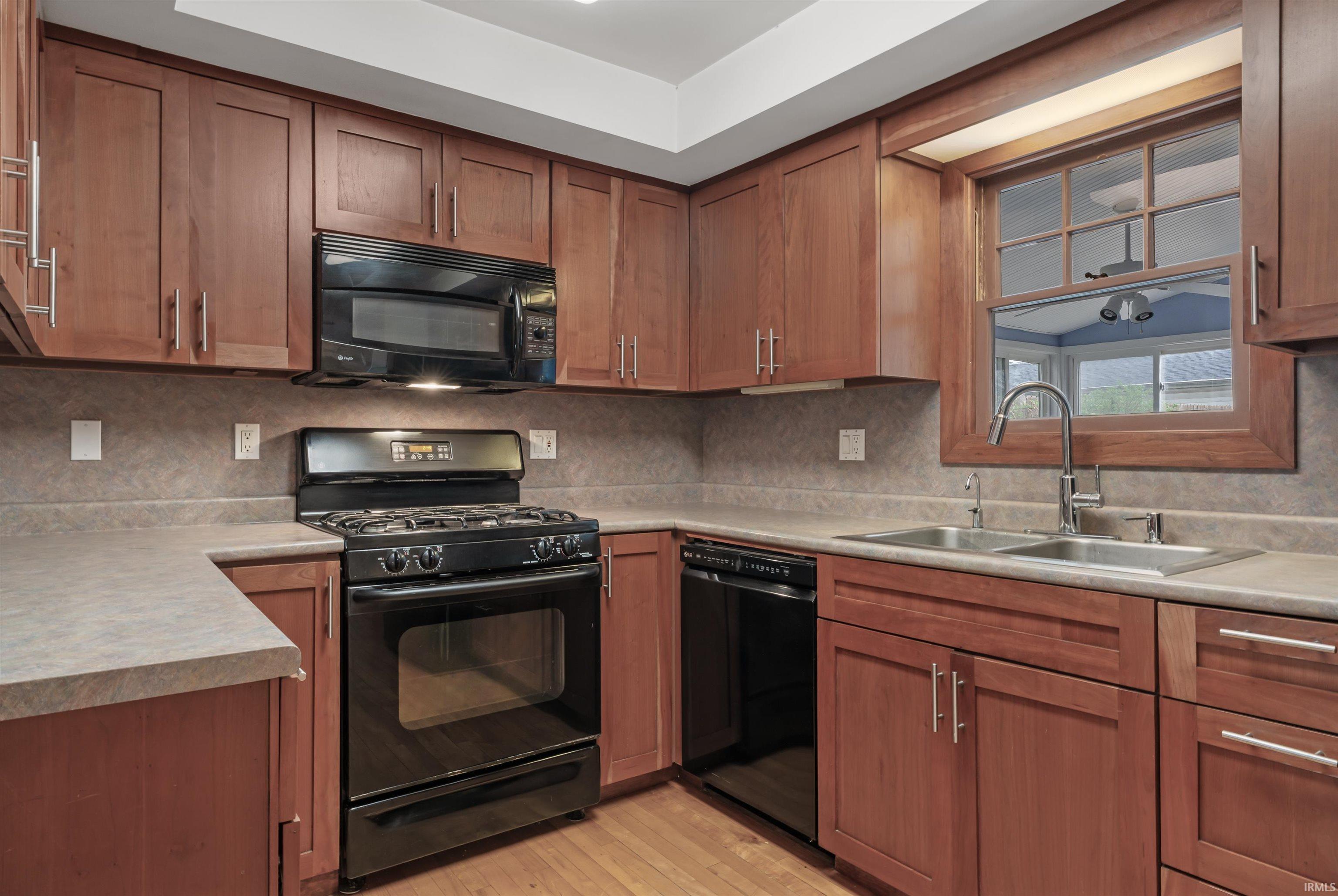 Kitchen featuring black appliances, light countertops, wood finish cabinetry, backsplash, and light wood-style floors