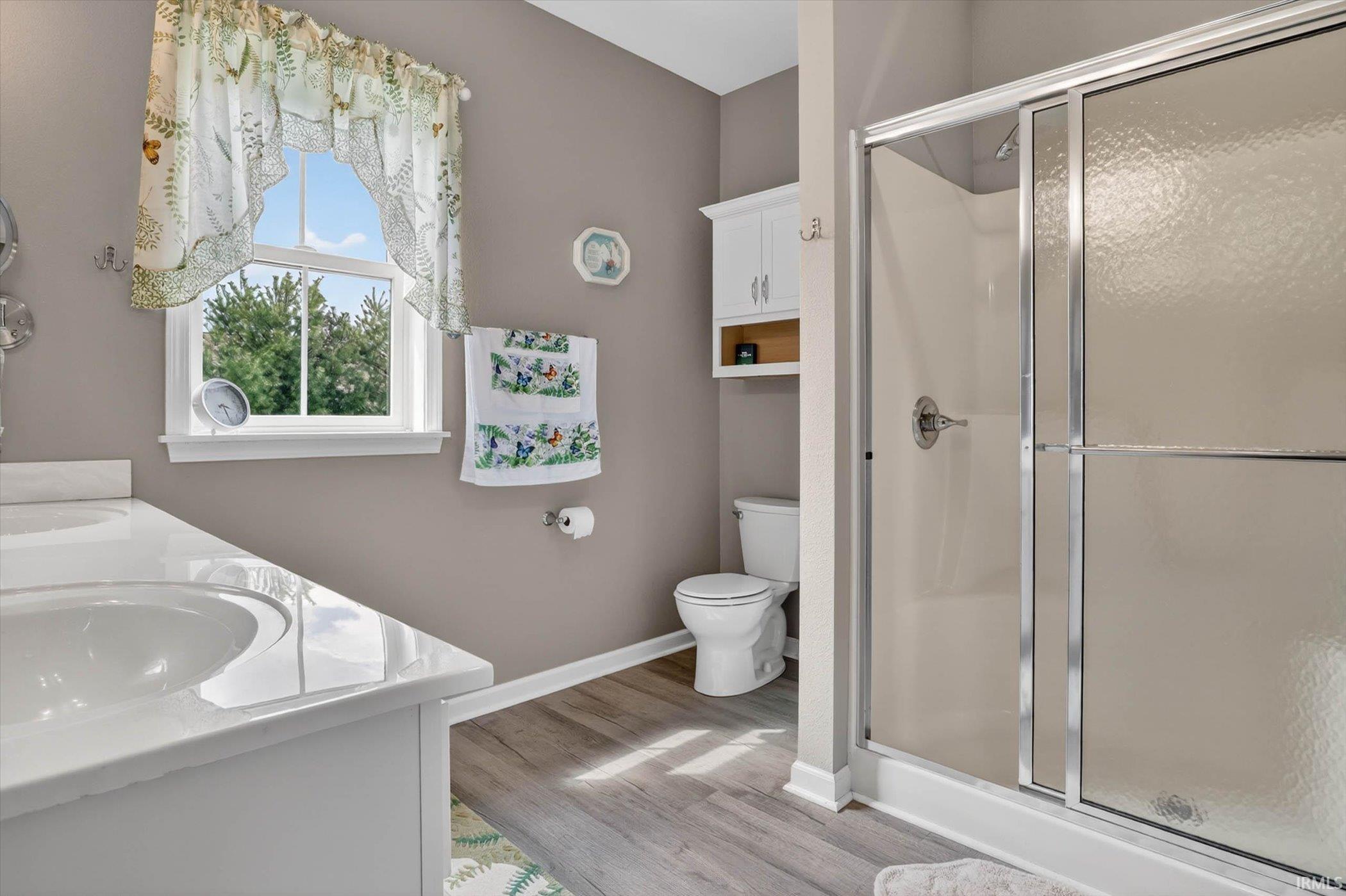 Full bath featuring double vanity, a stall shower, and light wood-style floors