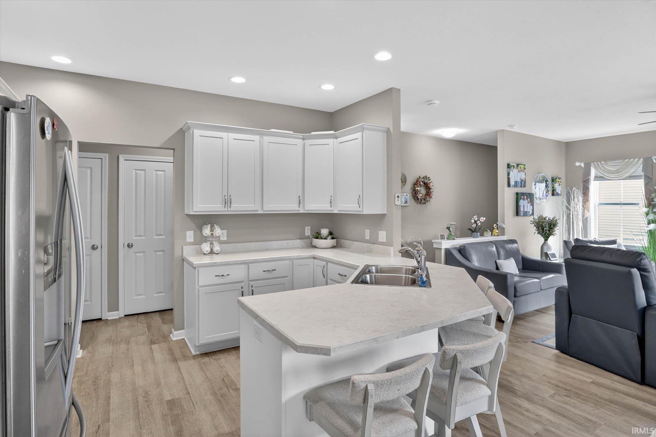 Kitchen featuring open floor plan, stainless steel refrigerator with ice dispenser, a peninsula, light countertops, and a kitchen breakfast bar