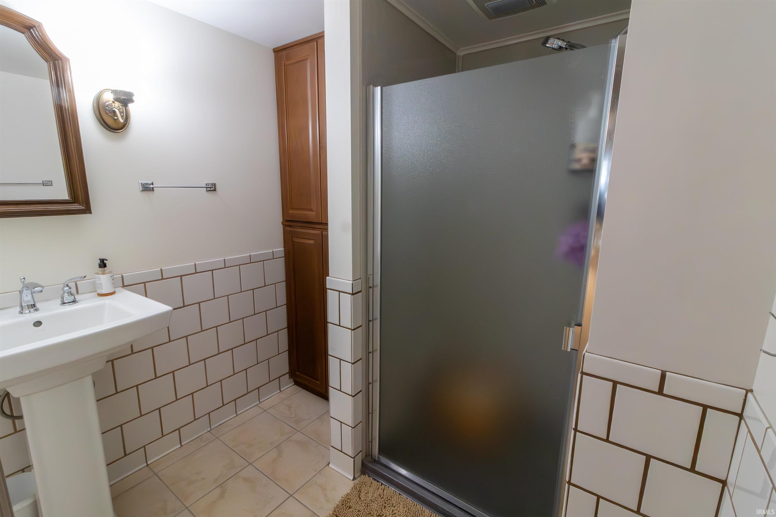 Bathroom featuring tile walls, a shower stall, a wainscoted wall, and light tile patterned floors