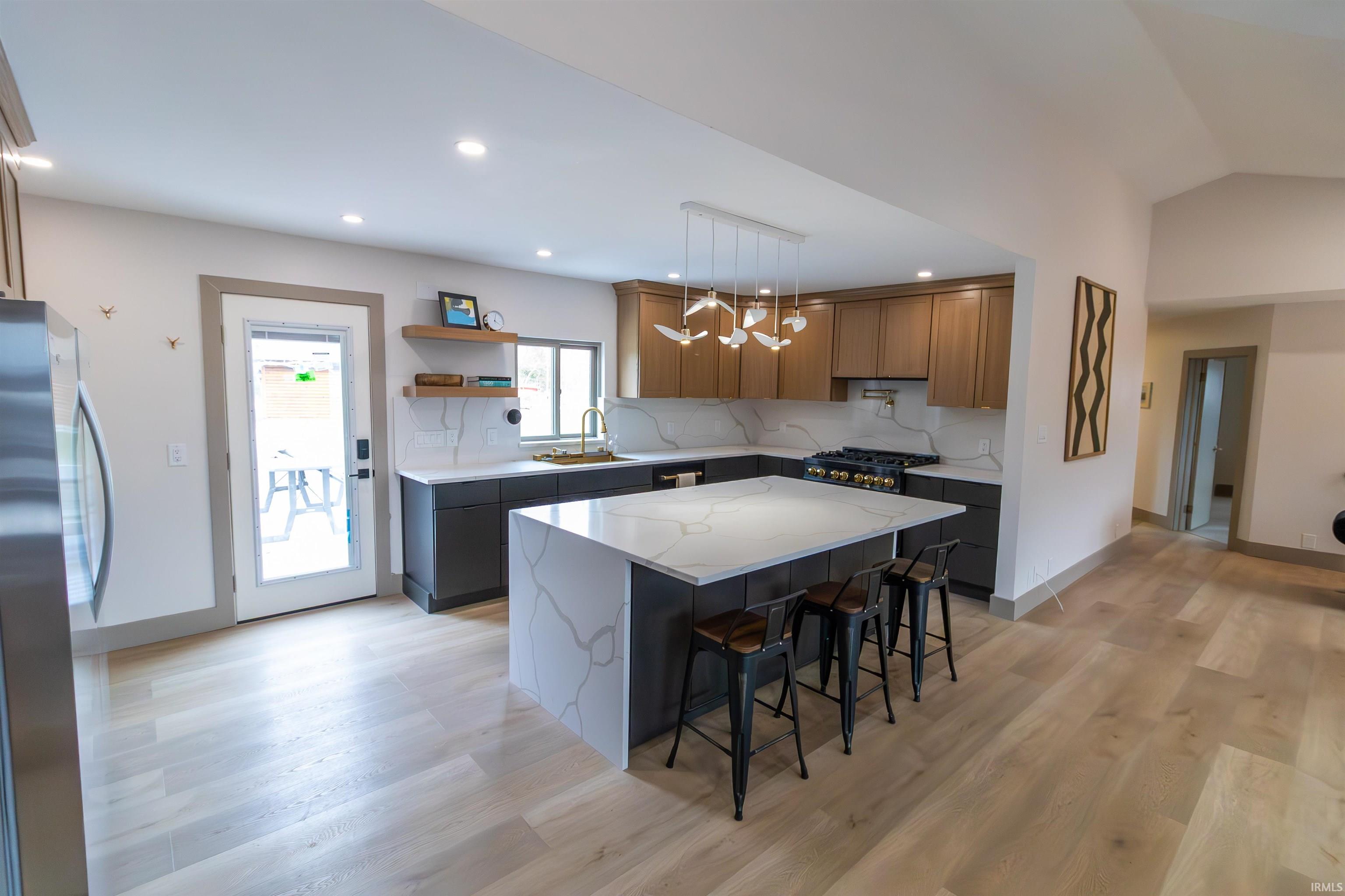 Two tone kitchen featuring light stone countertops, freestanding refrigerator, a kitchen bar, a center island, and open shelves